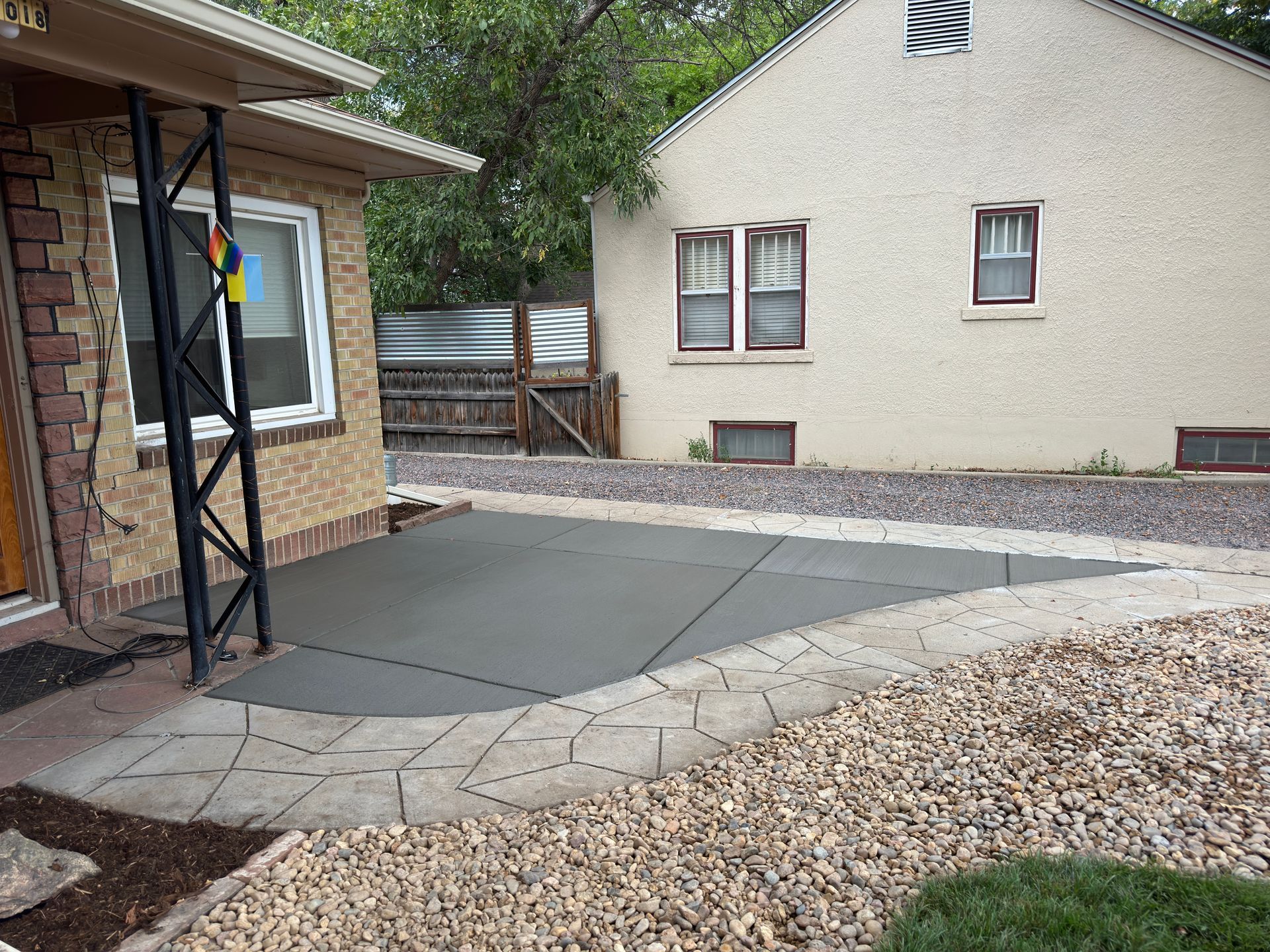 Newly poured concrete patio next to a tan house with decorative stone border and gravel.