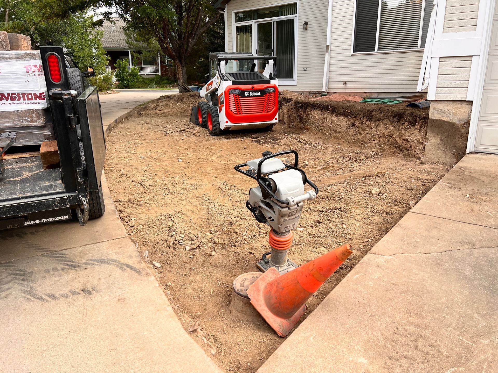 Construction site with a Bobcat, compactor, and orange safety cone.