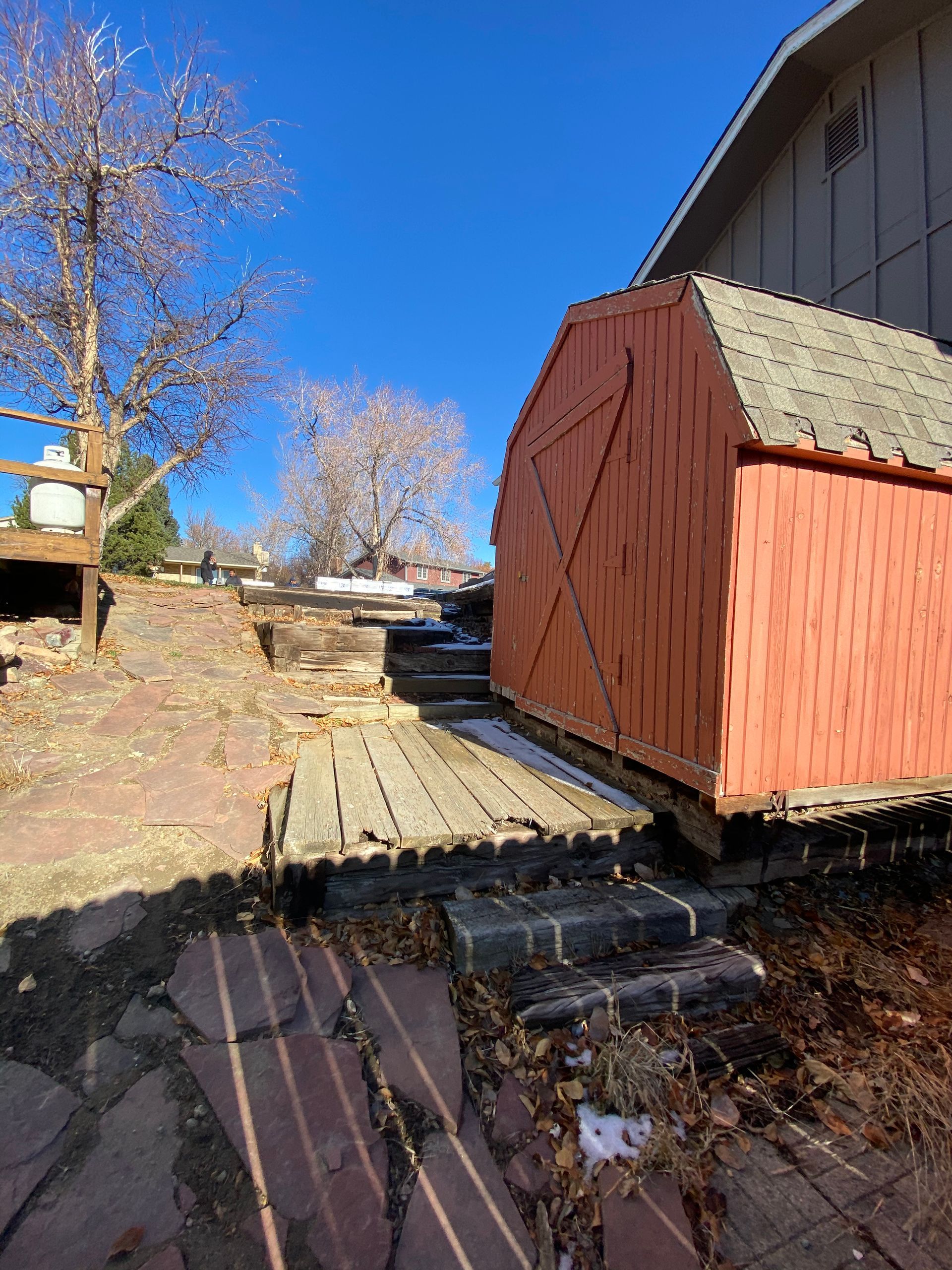 Red shed on raised brick patio, wooden walkway, blue sky.