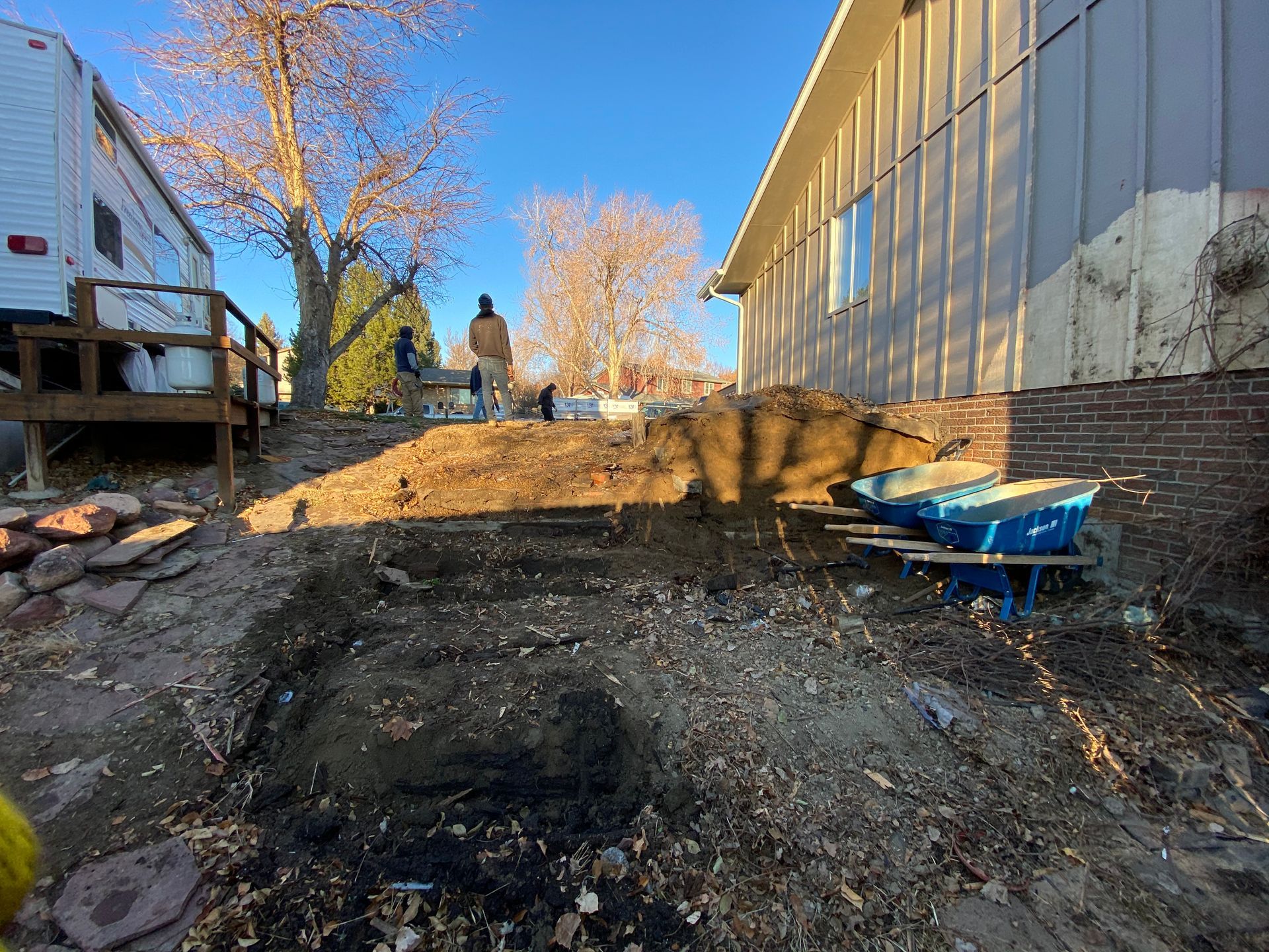 Workers excavating dirt in a yard near a house and a camper, creating steps.