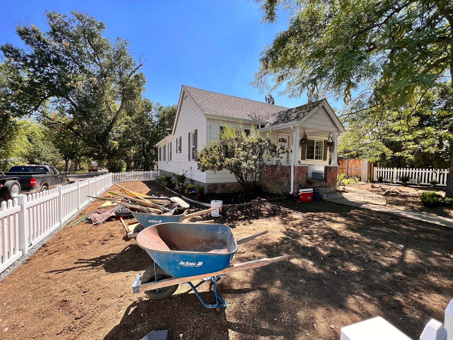 A house with a white fence and a wheelbarrow in the yard, likely under construction.