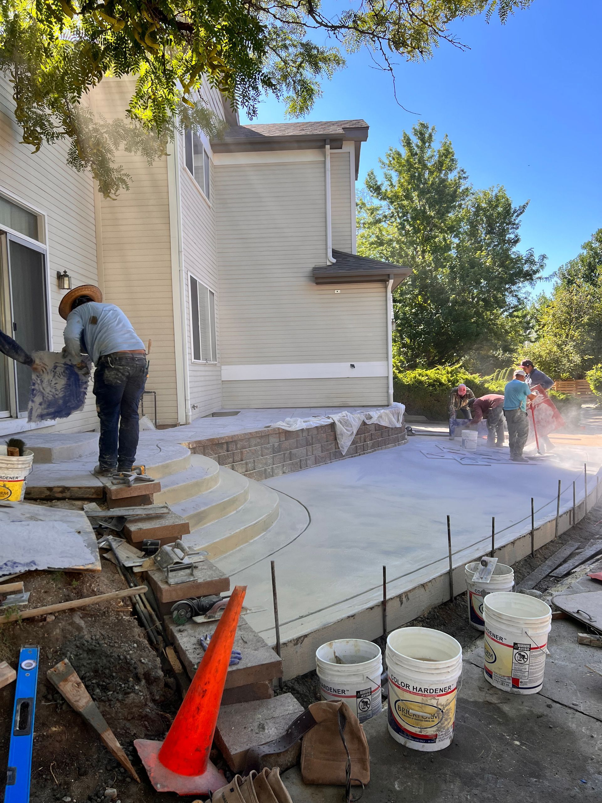 Construction workers pouring concrete for a patio next to a two-story beige house.