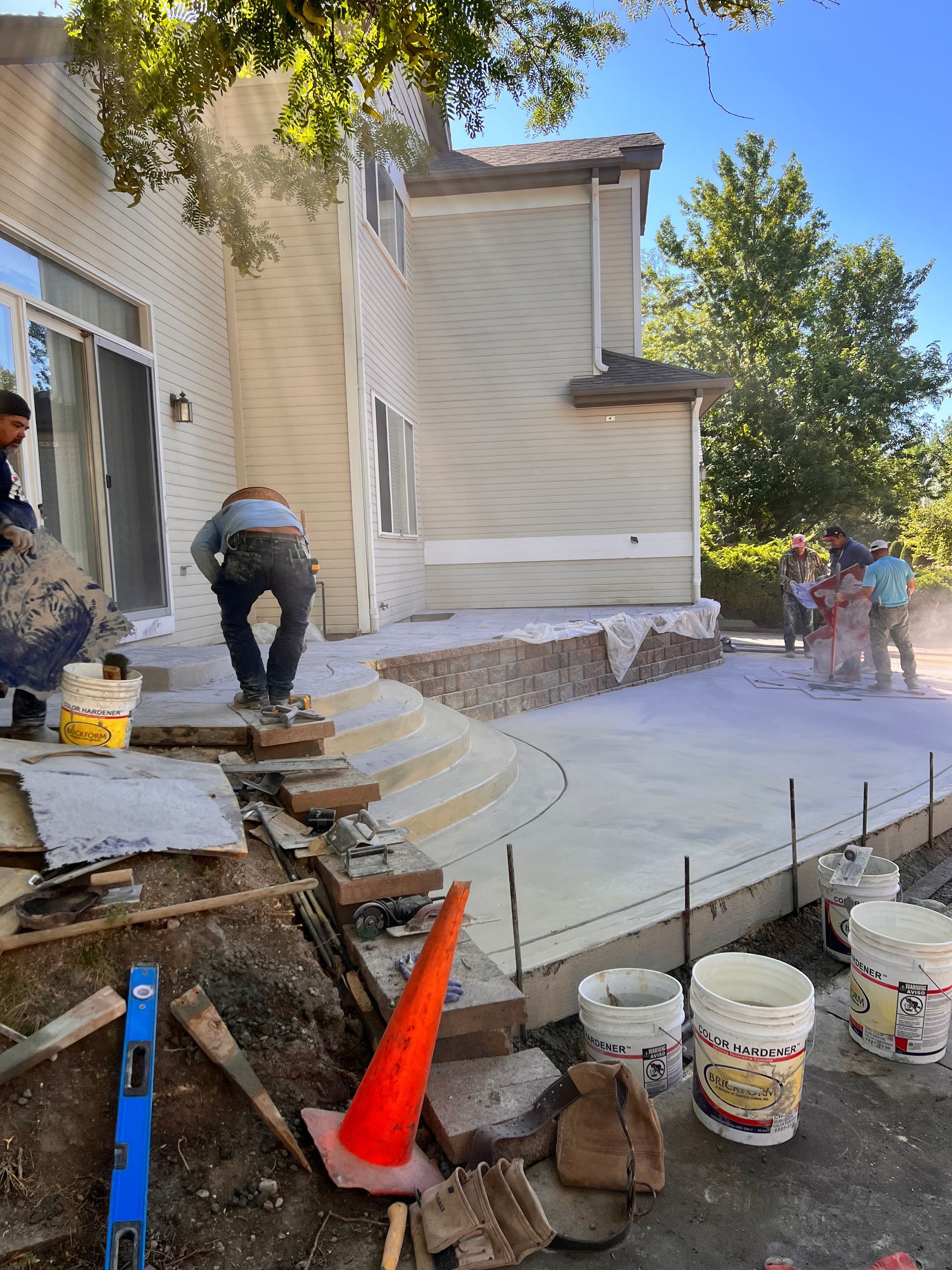 Construction workers pouring concrete for a patio next to a two-story beige house.