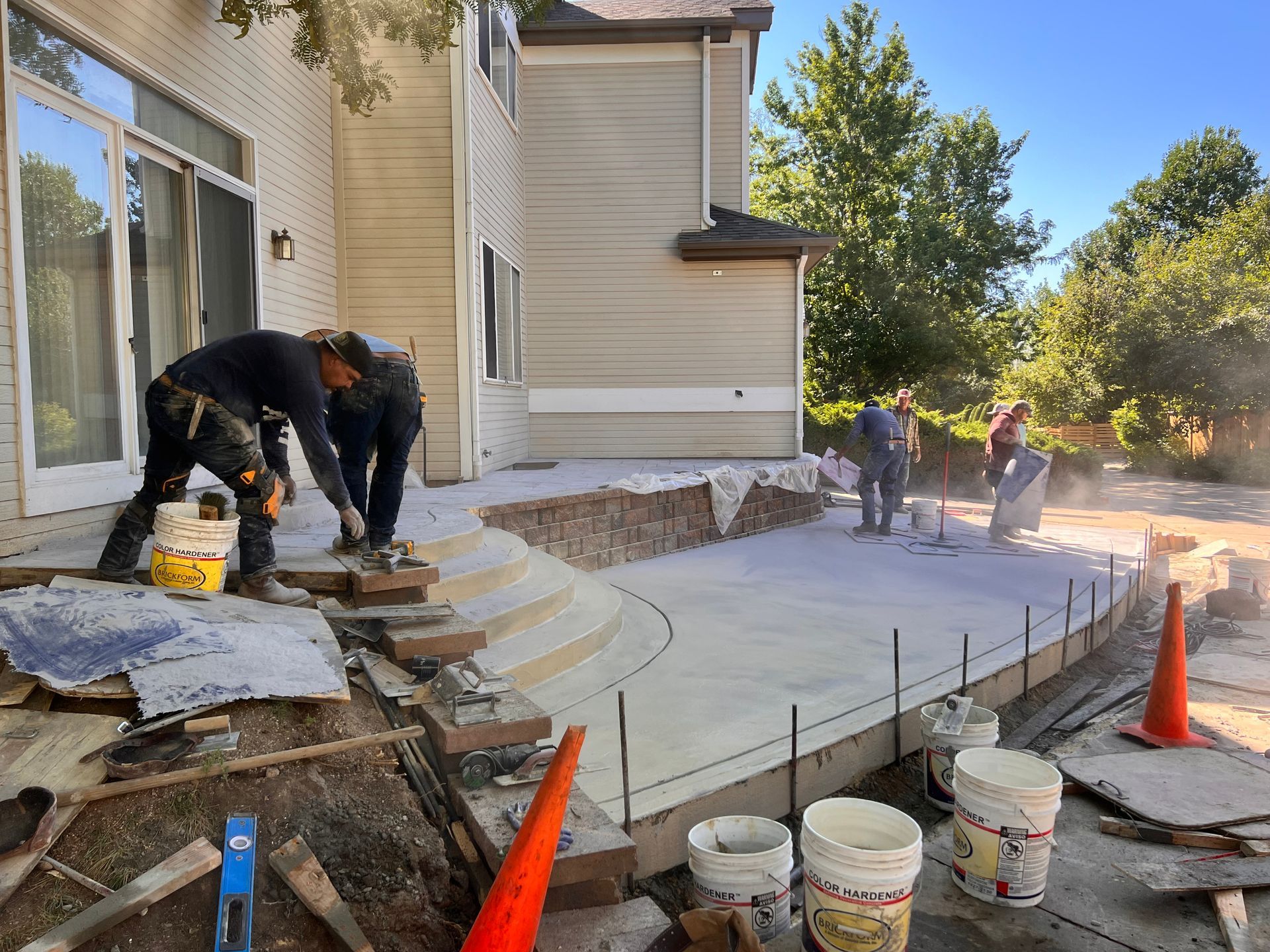 Construction workers pouring concrete for a patio and steps next to a two-story house.