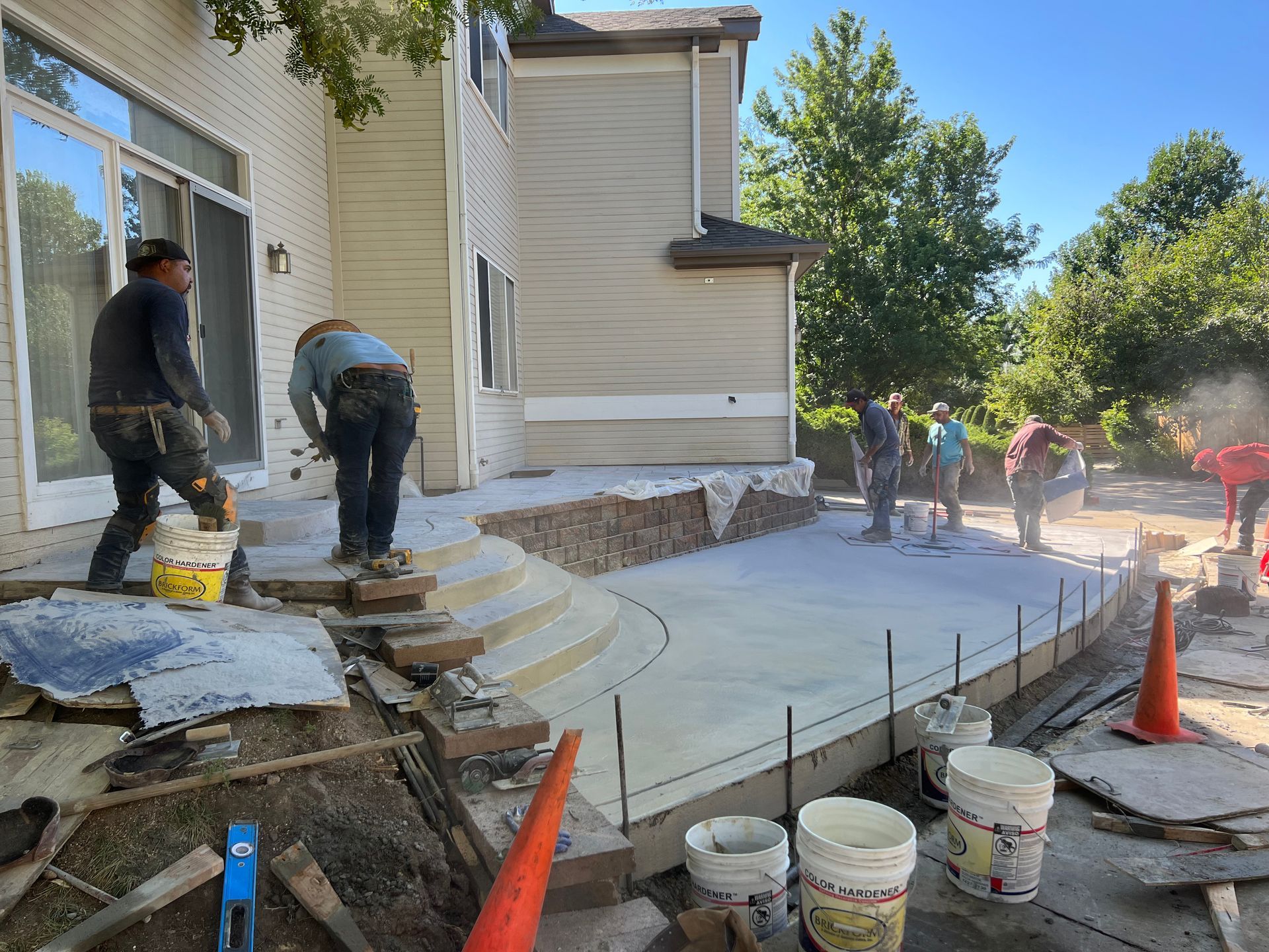 Construction workers pouring concrete for a patio next to a two-story house.