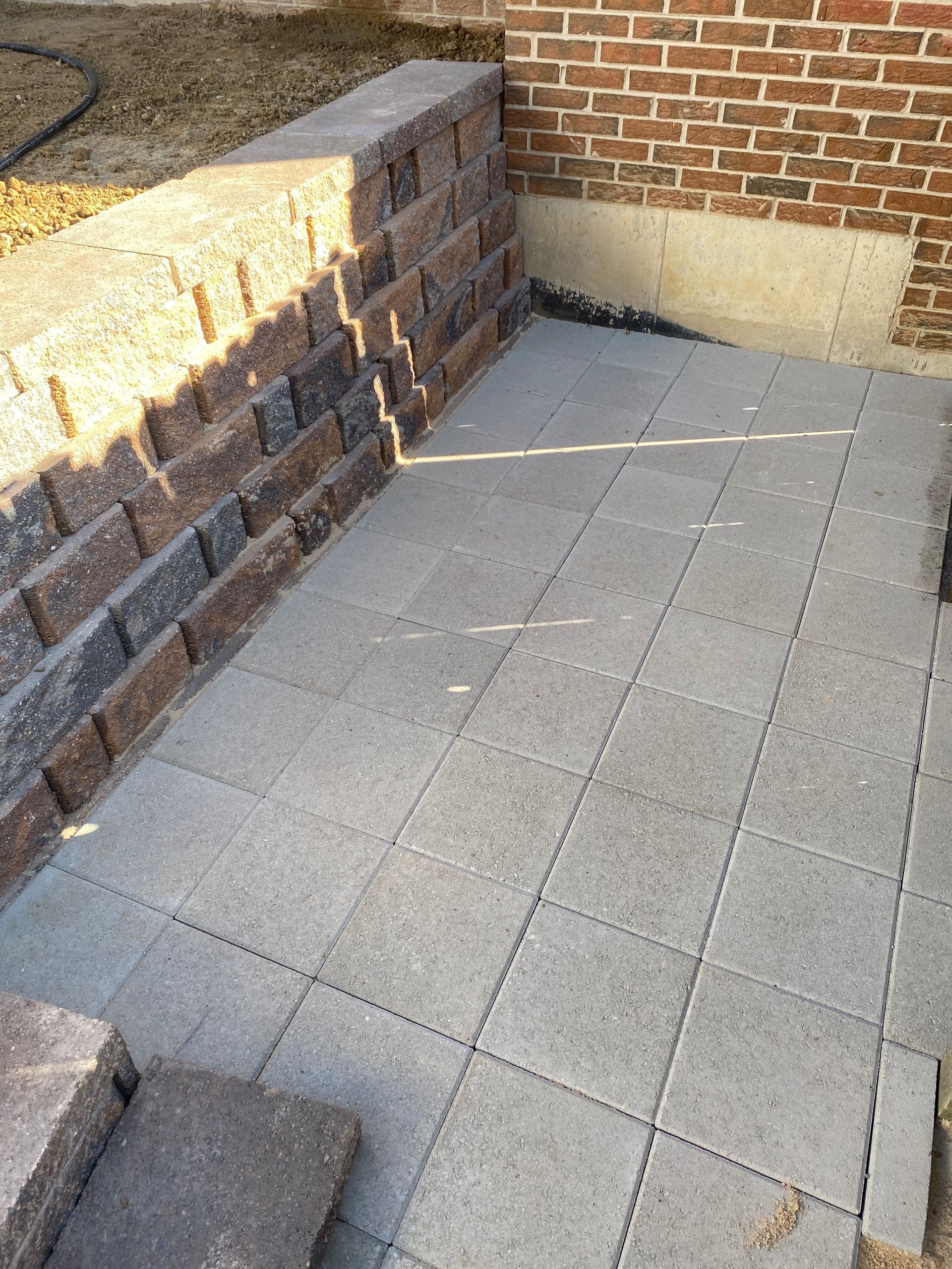 Concrete pavers being installed next to a brick retaining wall and a red brick building.