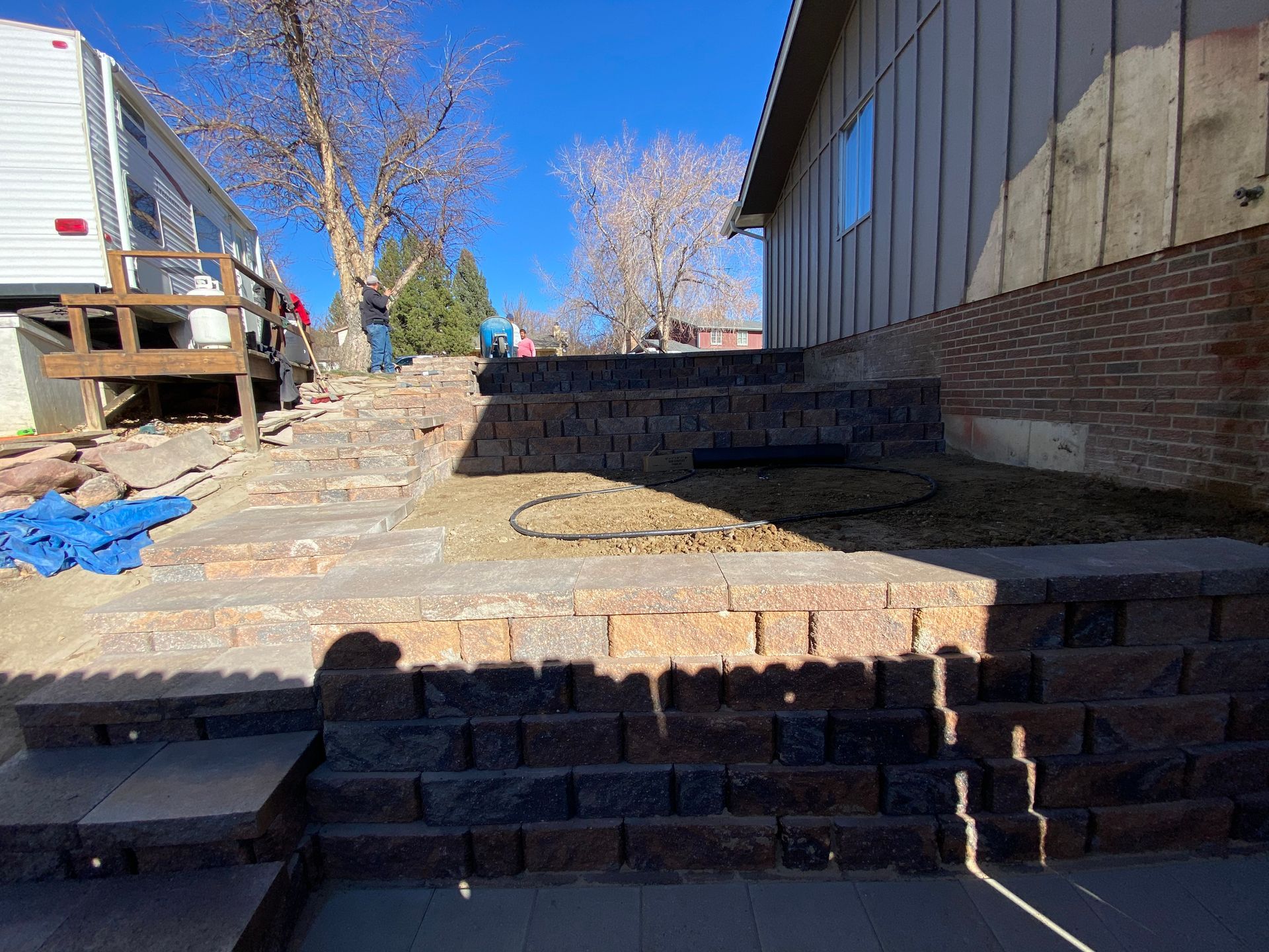 Stone retaining walls and steps in a yard, leading toward a house. Sunny day.