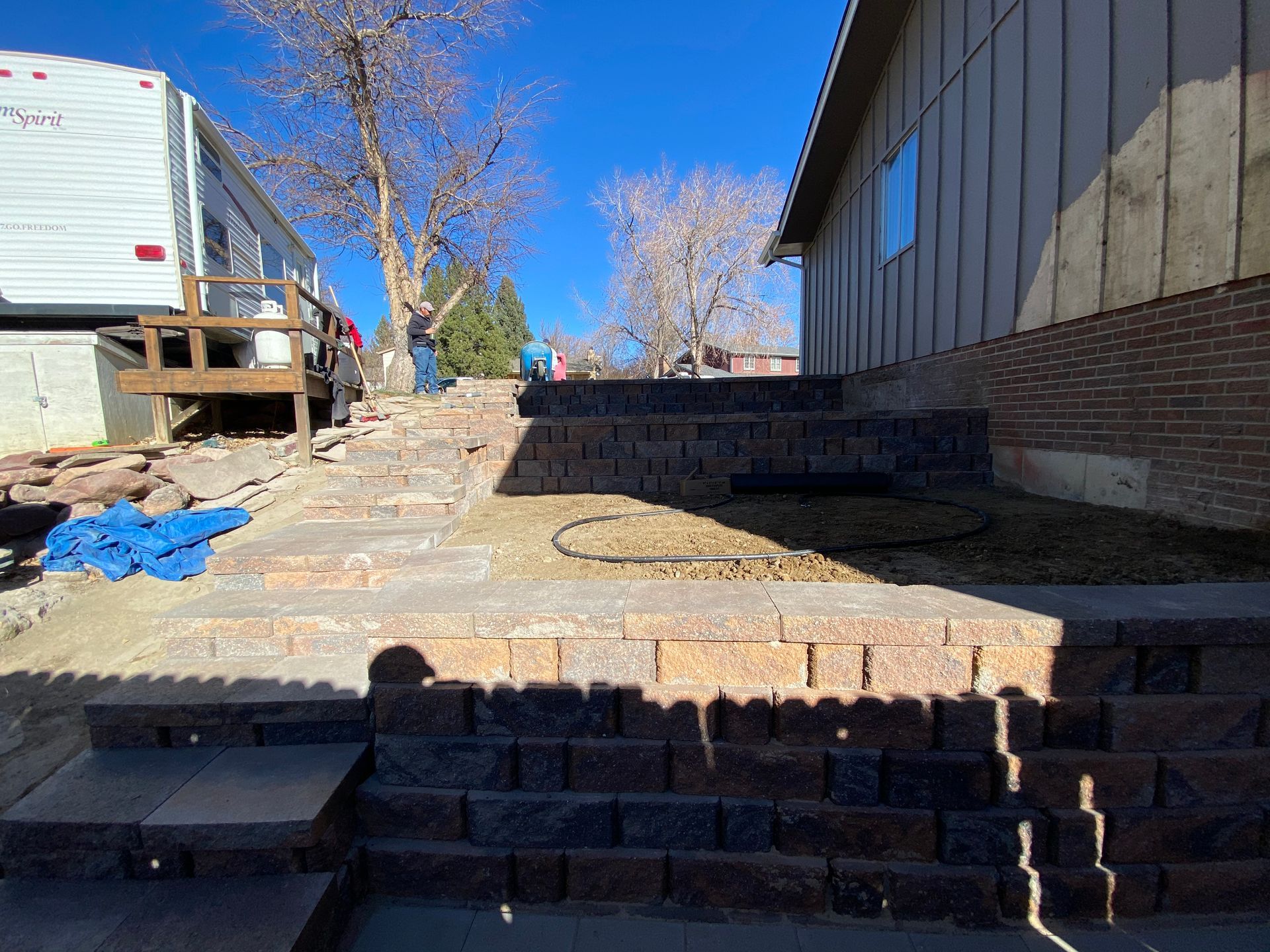 Brick retaining walls and steps on a sloped yard next to a house and RV on a sunny day.