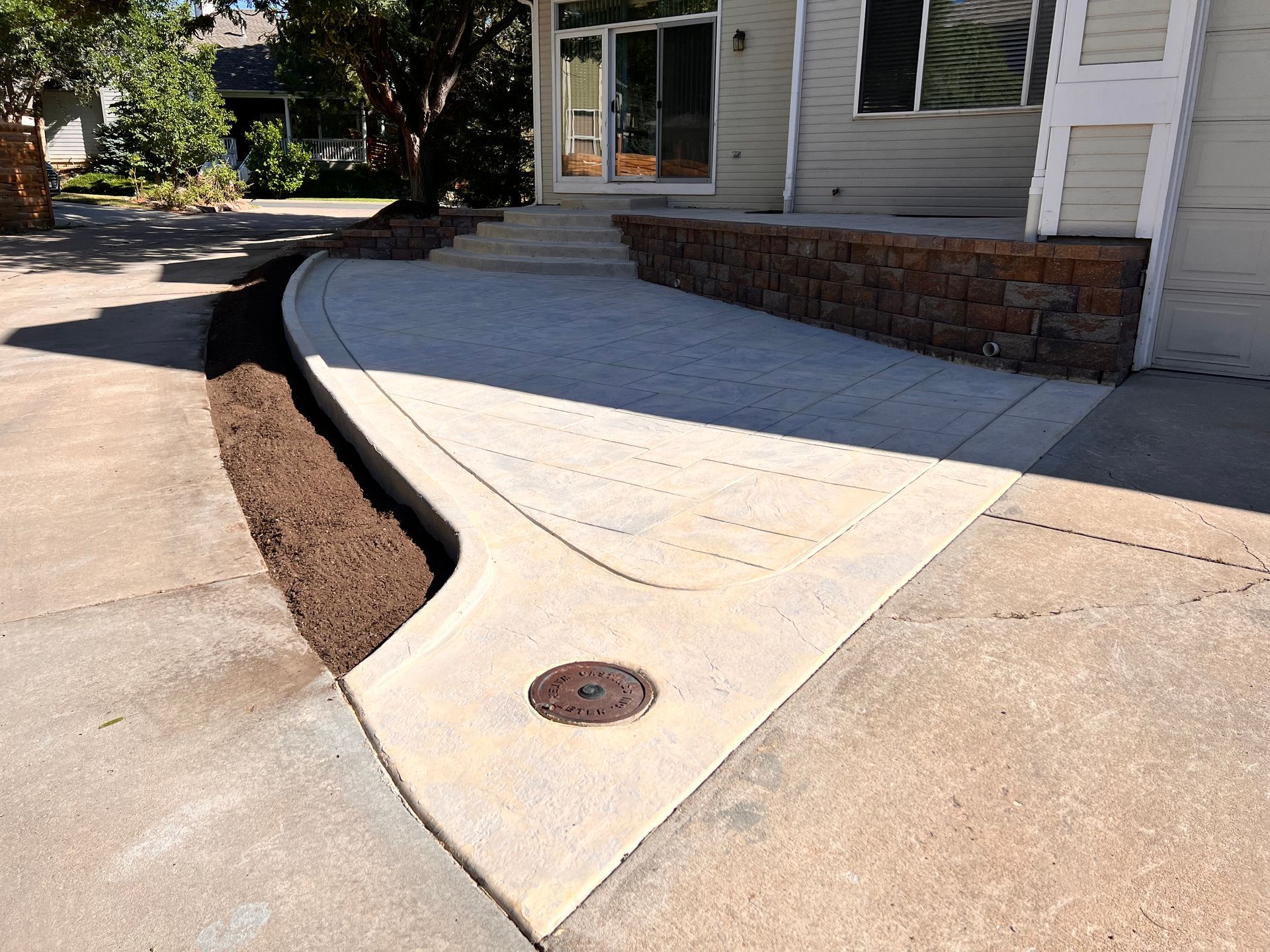 Concrete driveway leading to a house entrance with a retaining wall and mulch bed.