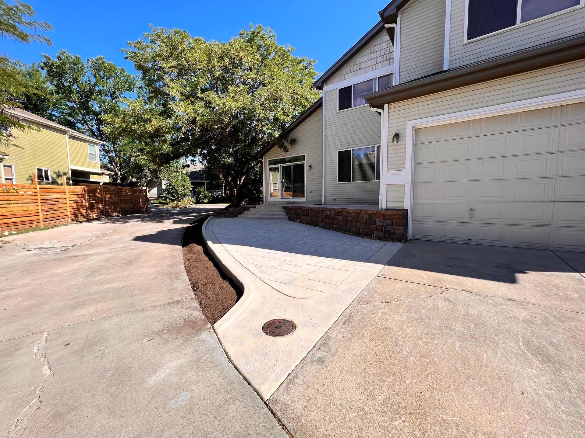 Driveway leading to a two-story beige house with a garage. Brown mulch borders the concrete.