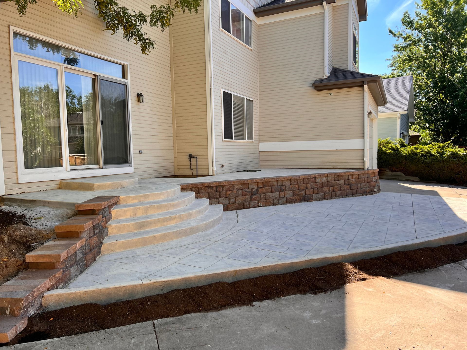 Tan house with a concrete patio, steps, and a low retaining wall.
