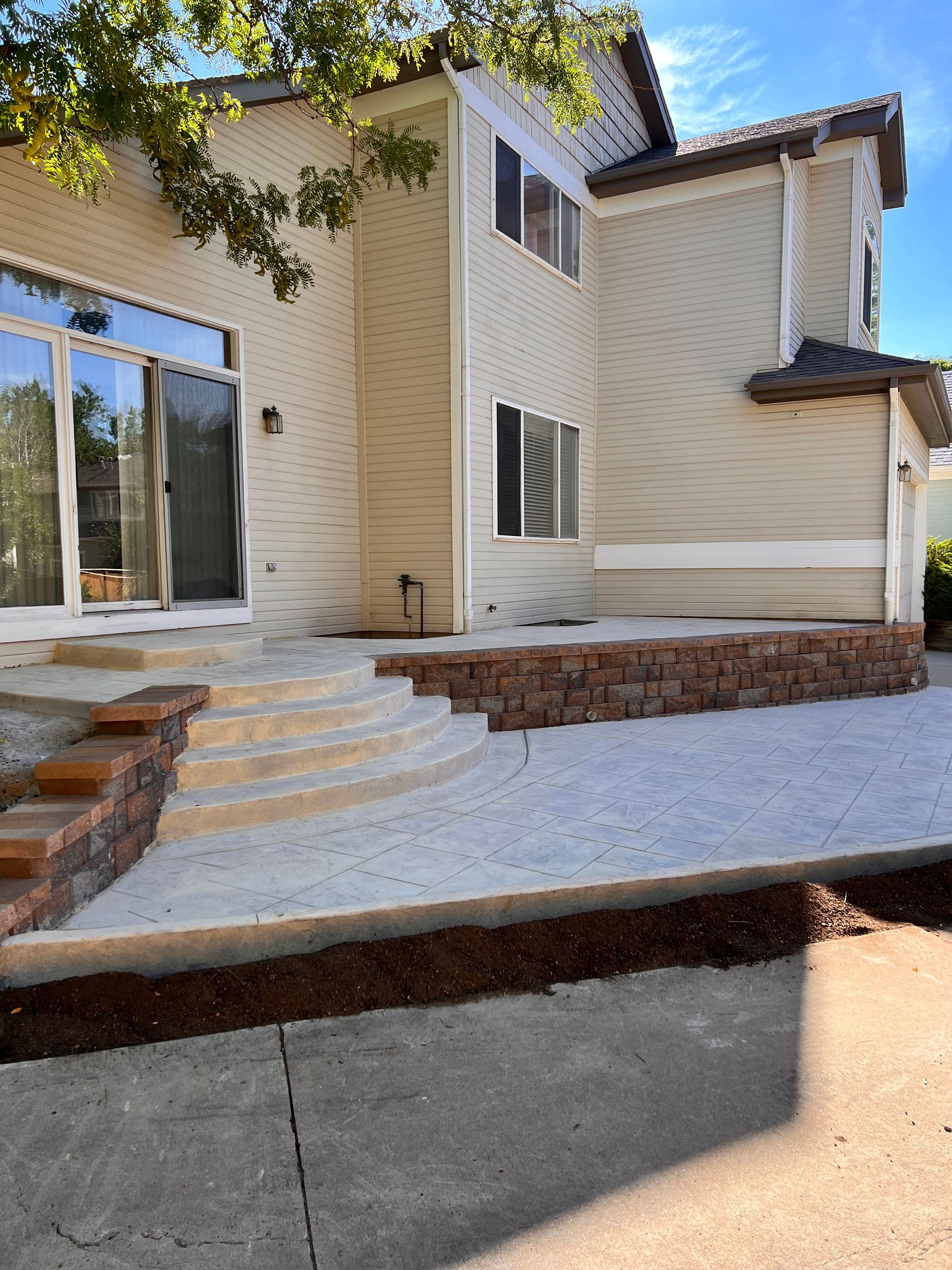 Two-story beige house with a concrete patio, steps, and red brick retaining wall.