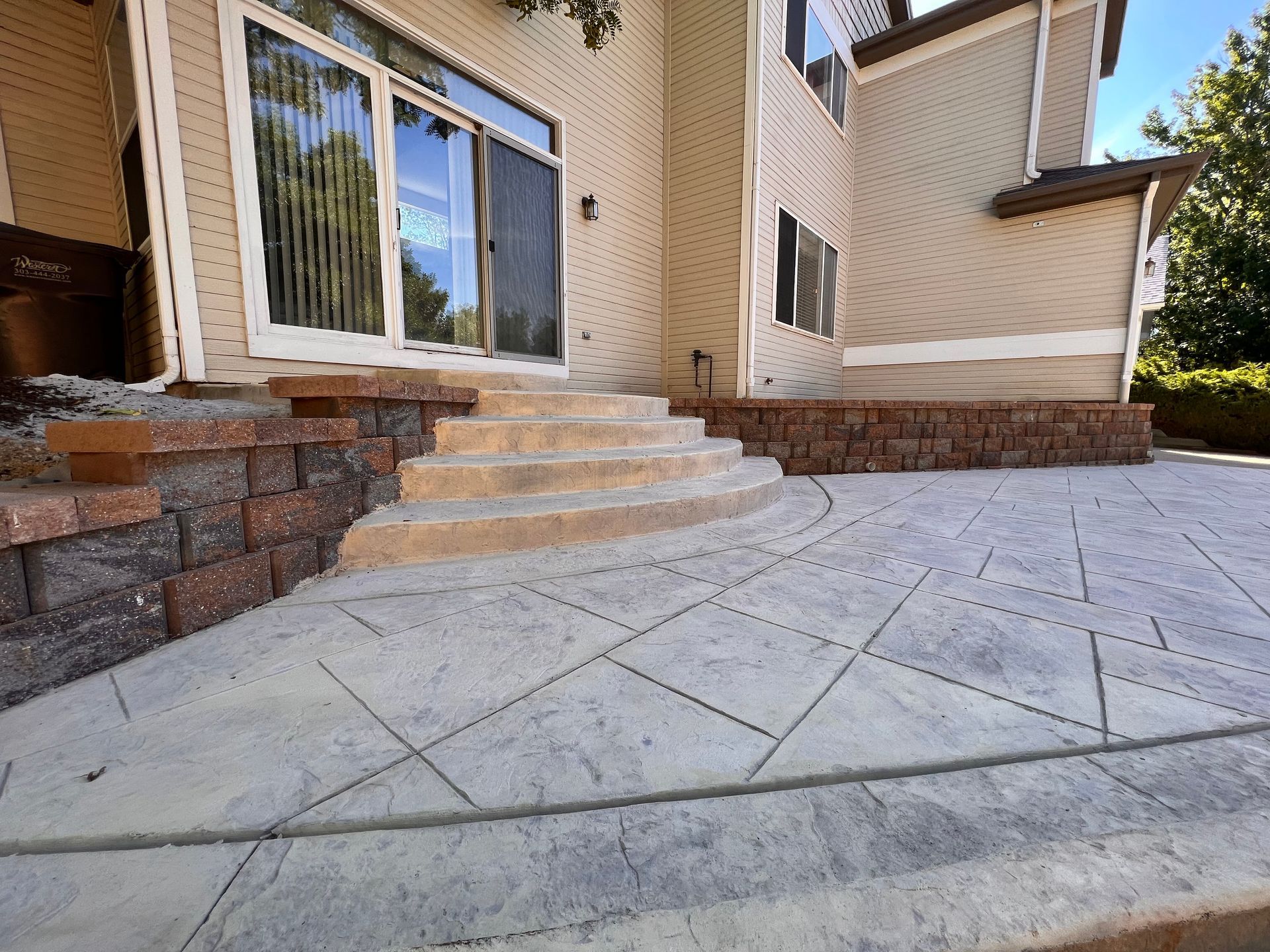 Concrete patio with steps leading to a house, featuring brick retaining walls.