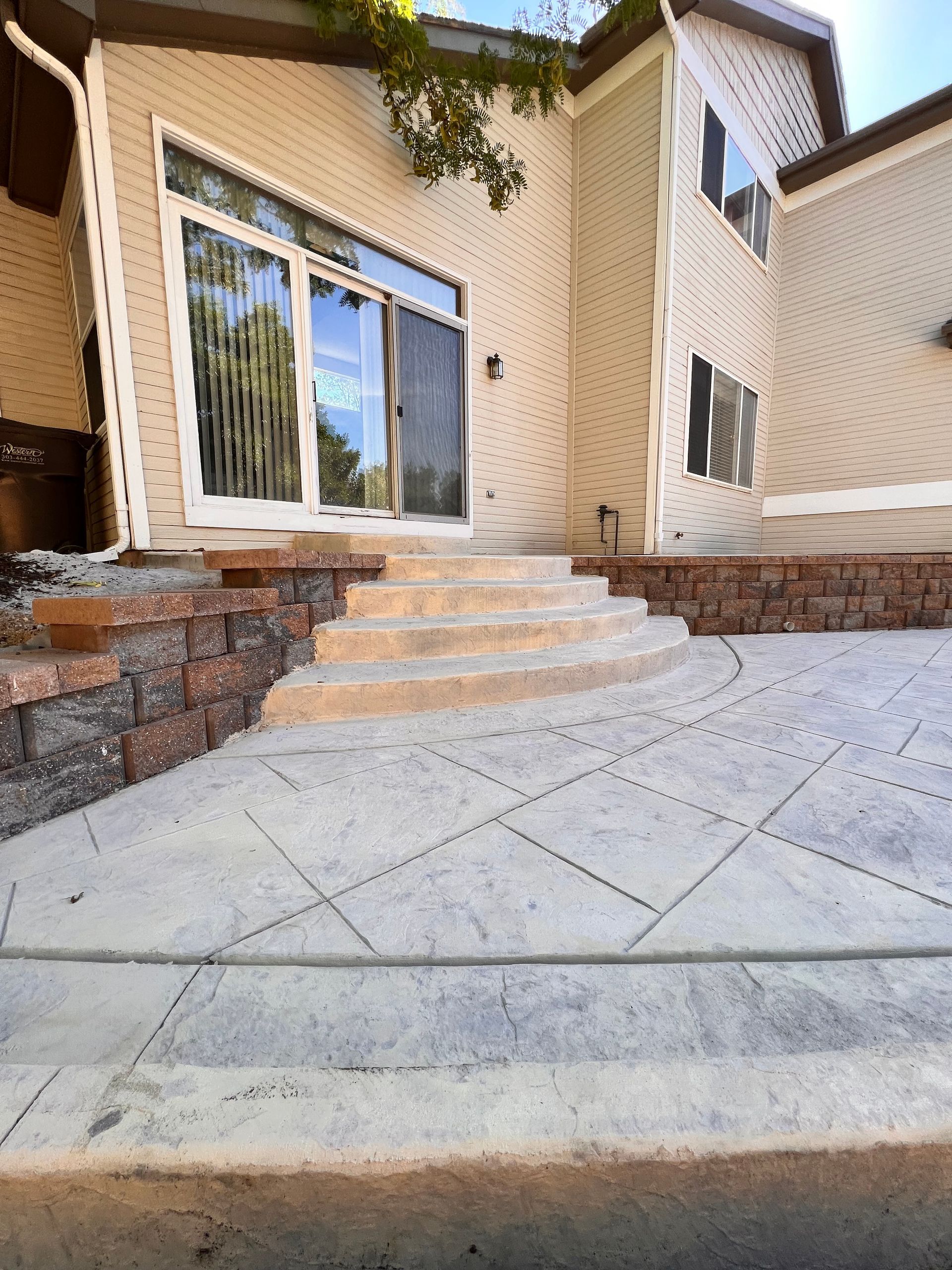Concrete patio with brick retaining walls and steps leading to a sliding glass door.