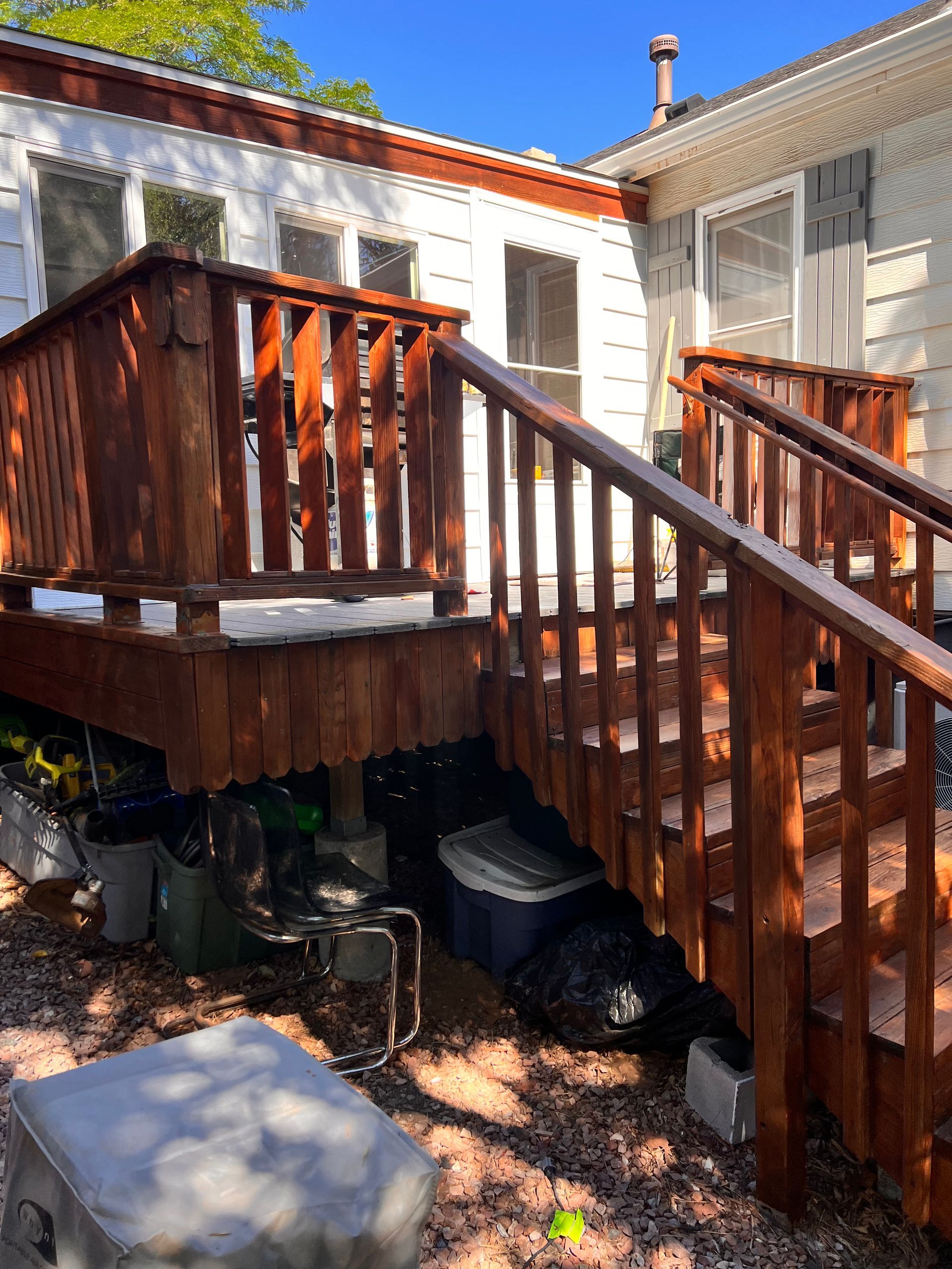 Wooden deck with stairs, stained brown, attached to a white house.