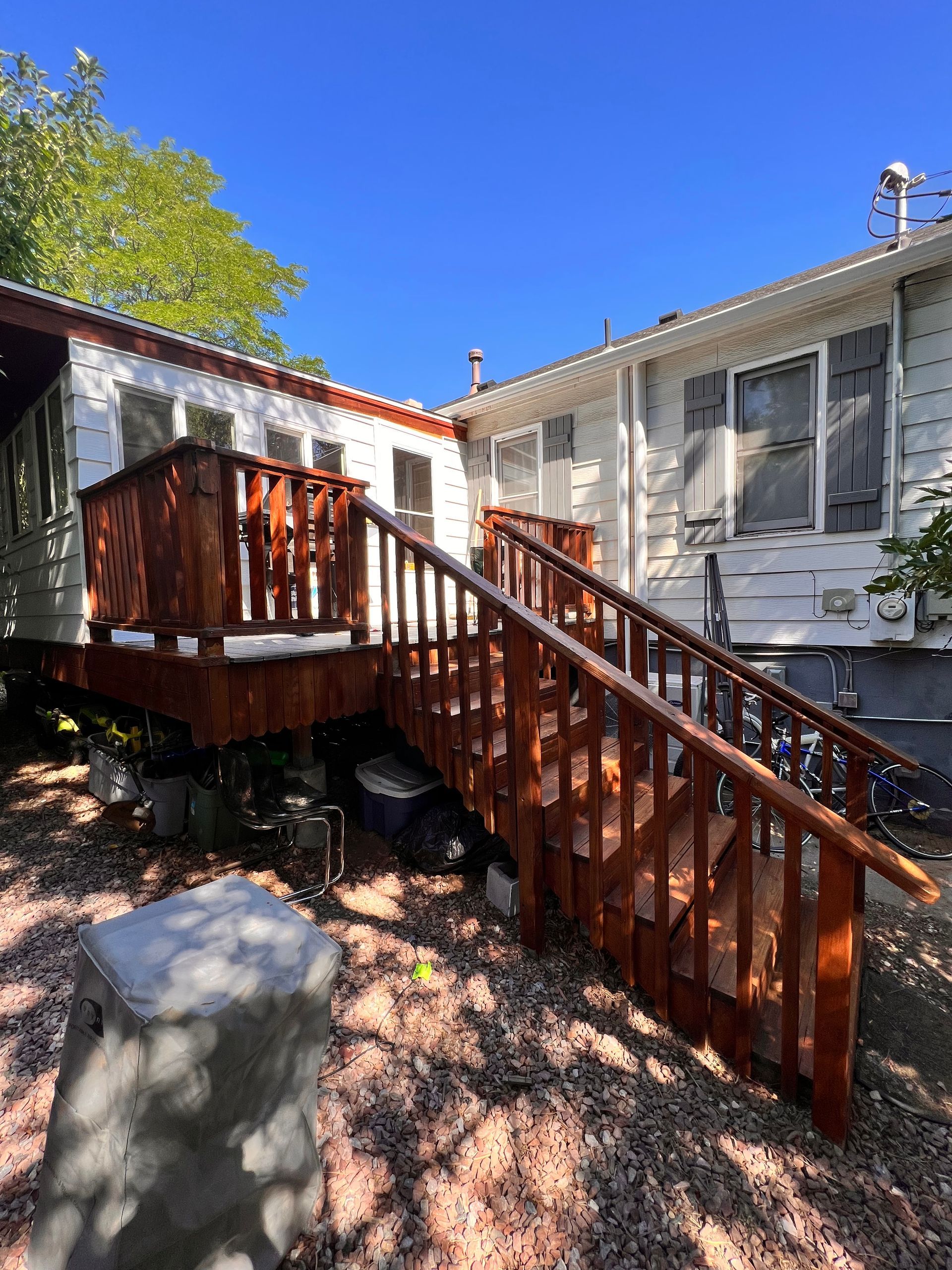 Wooden deck with stairs leads to a white house under a clear, blue sky.