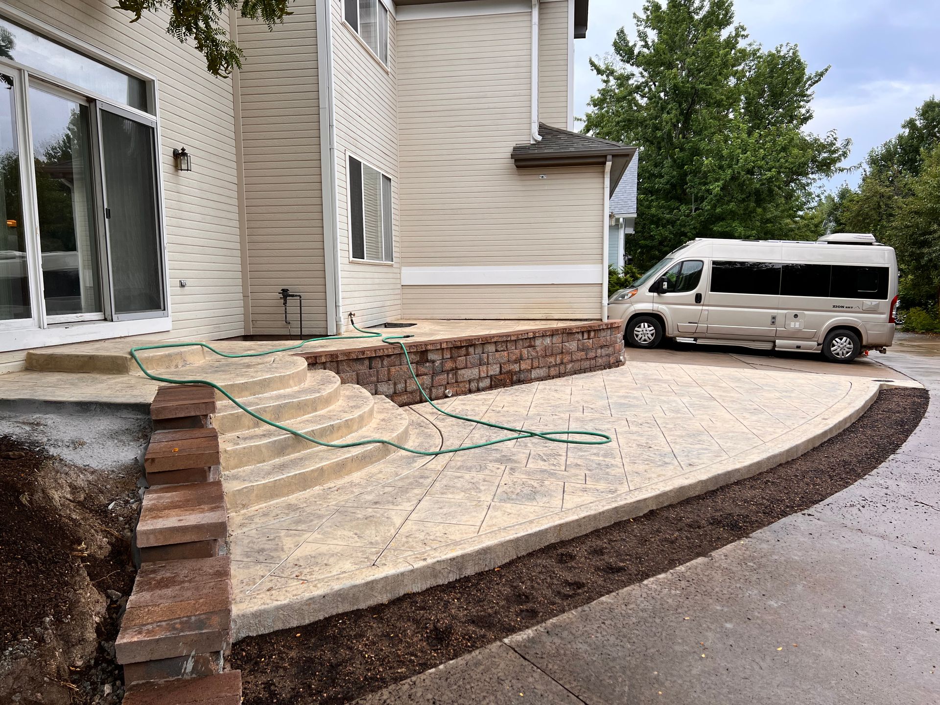 Curved patio with brick accents and steps, beside a light-colored building. A van is parked on the driveway.