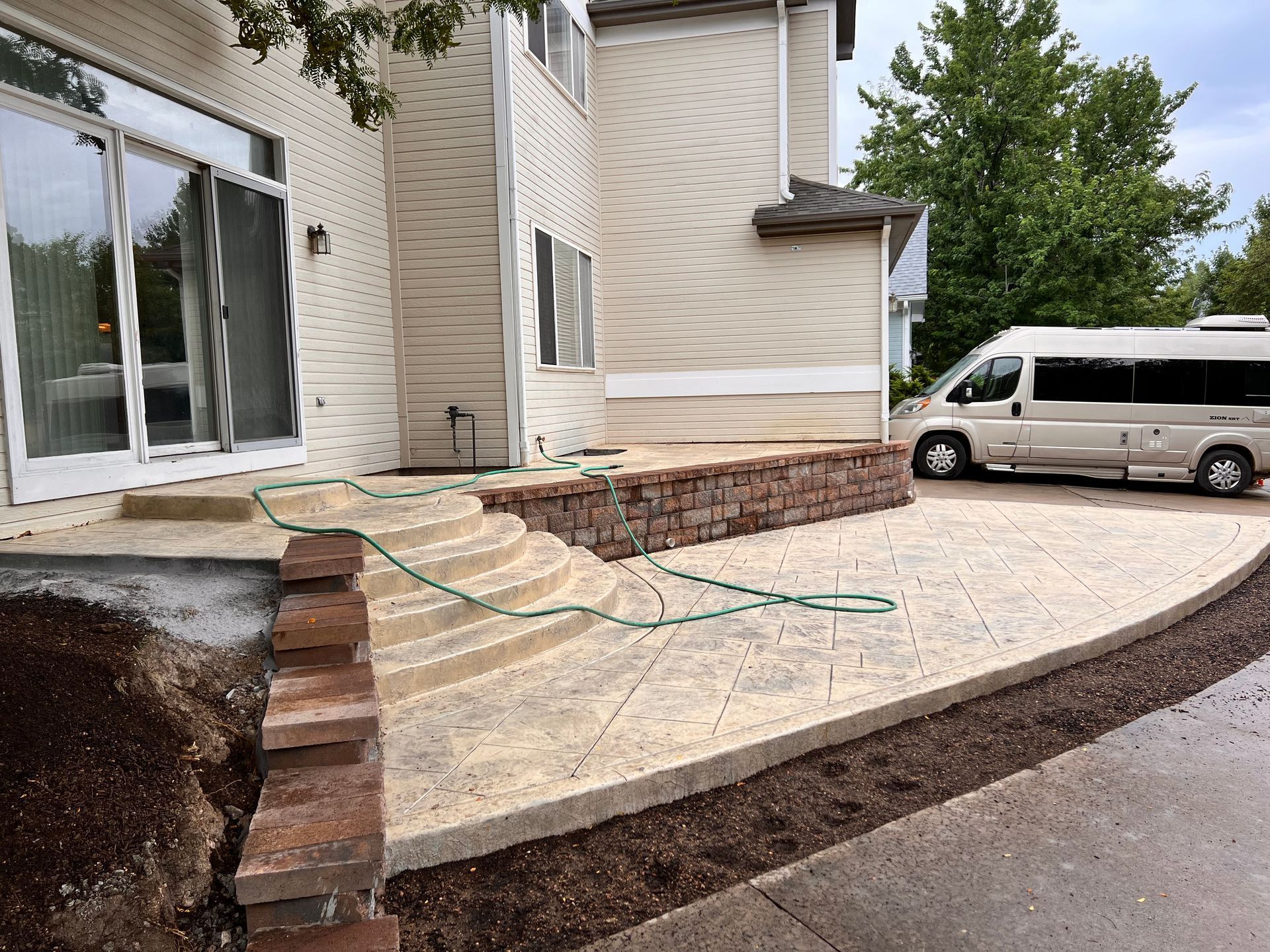 Concrete patio with steps, retaining wall, and a van parked beside a multi-story house.