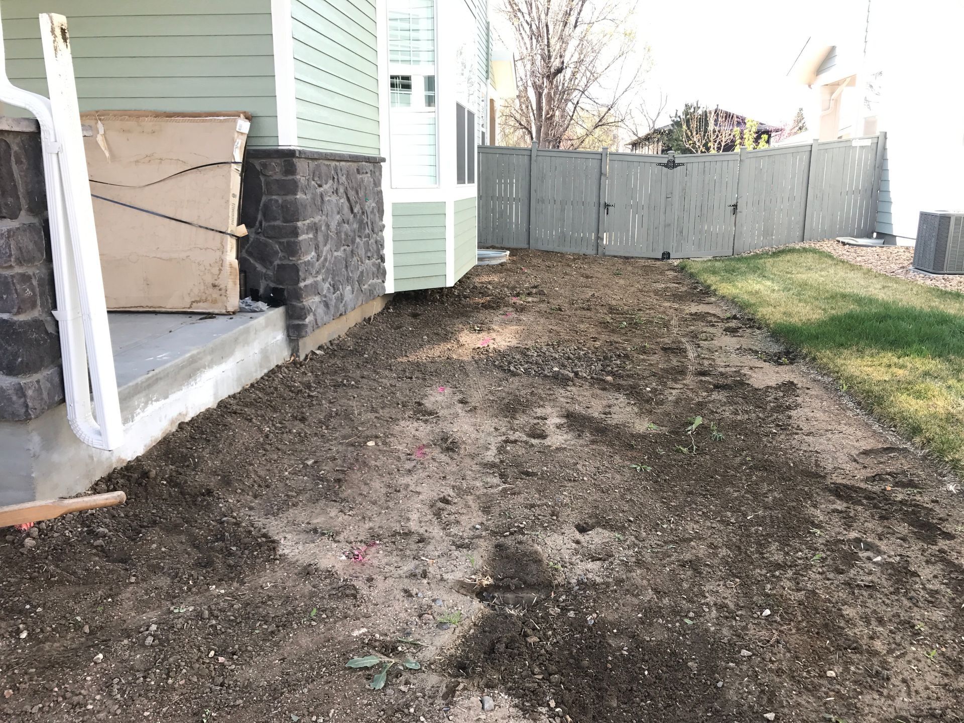 A dirt patch next to a house with a green facade, leading to a fence.
