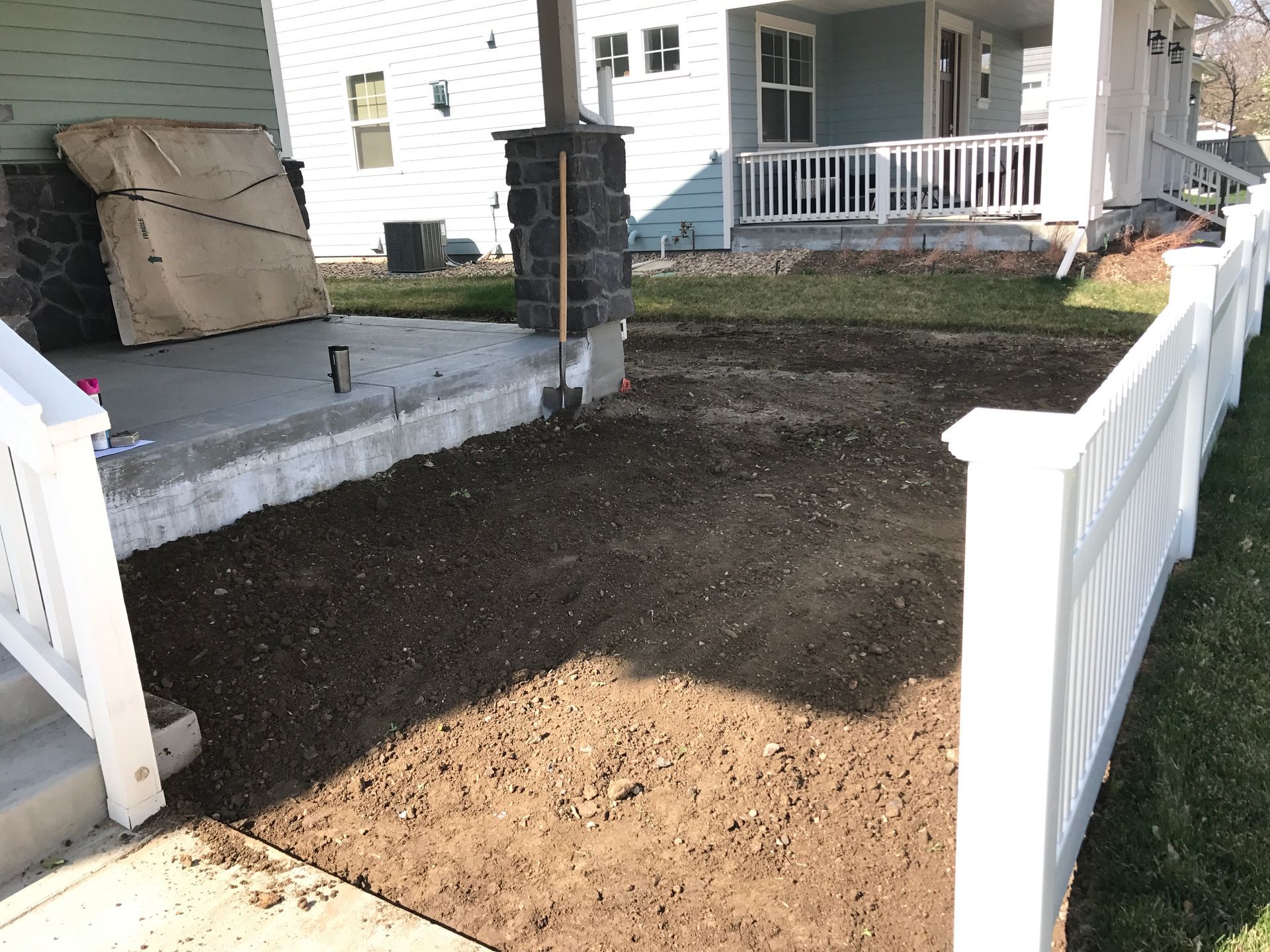Gravel yard in front of a porch with white railing and fence. A home with light blue siding is in the background.
