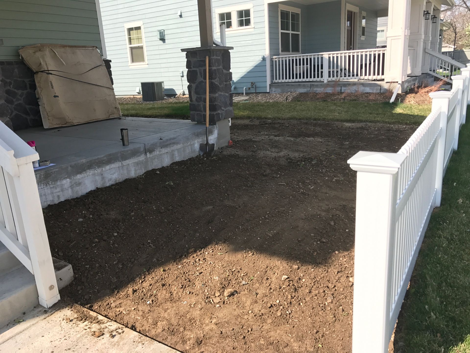 A porch with a newly laid dirt area between white fences, the house painted blue.