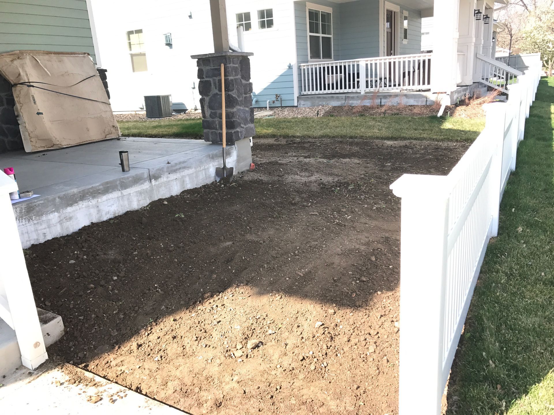 Gravel patch in front of a light blue house, bordered by white fence and concrete porch.