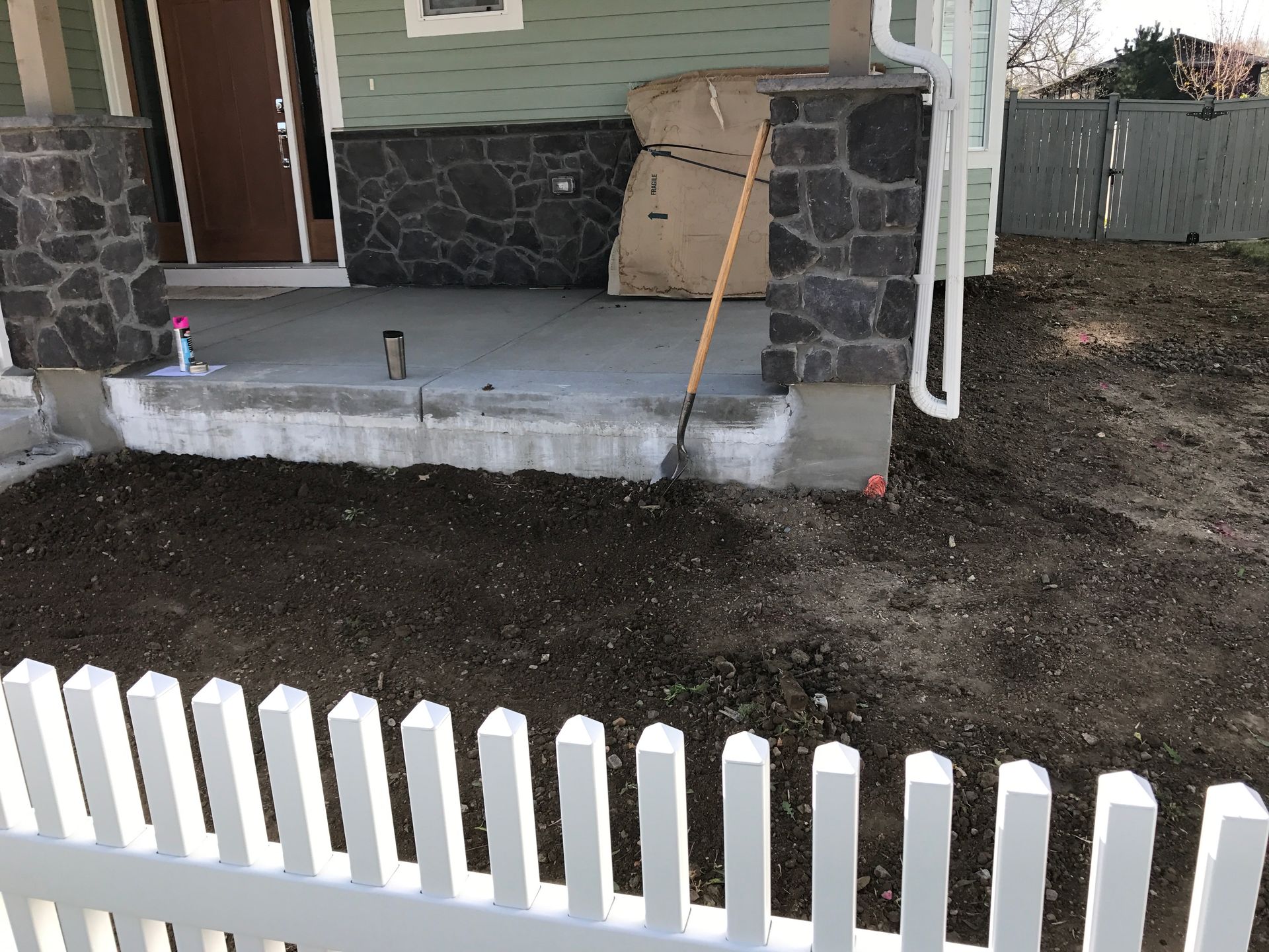 White picket fence in front of a porch with stone columns and dirt yard.