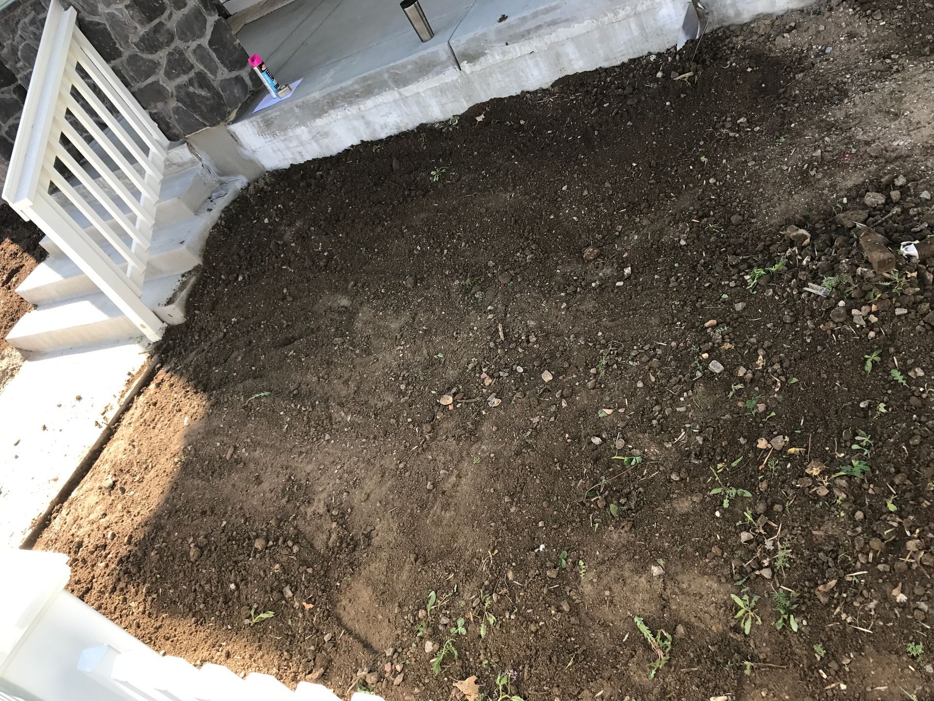 Brown soil patch next to white railing and concrete steps, ready for planting.