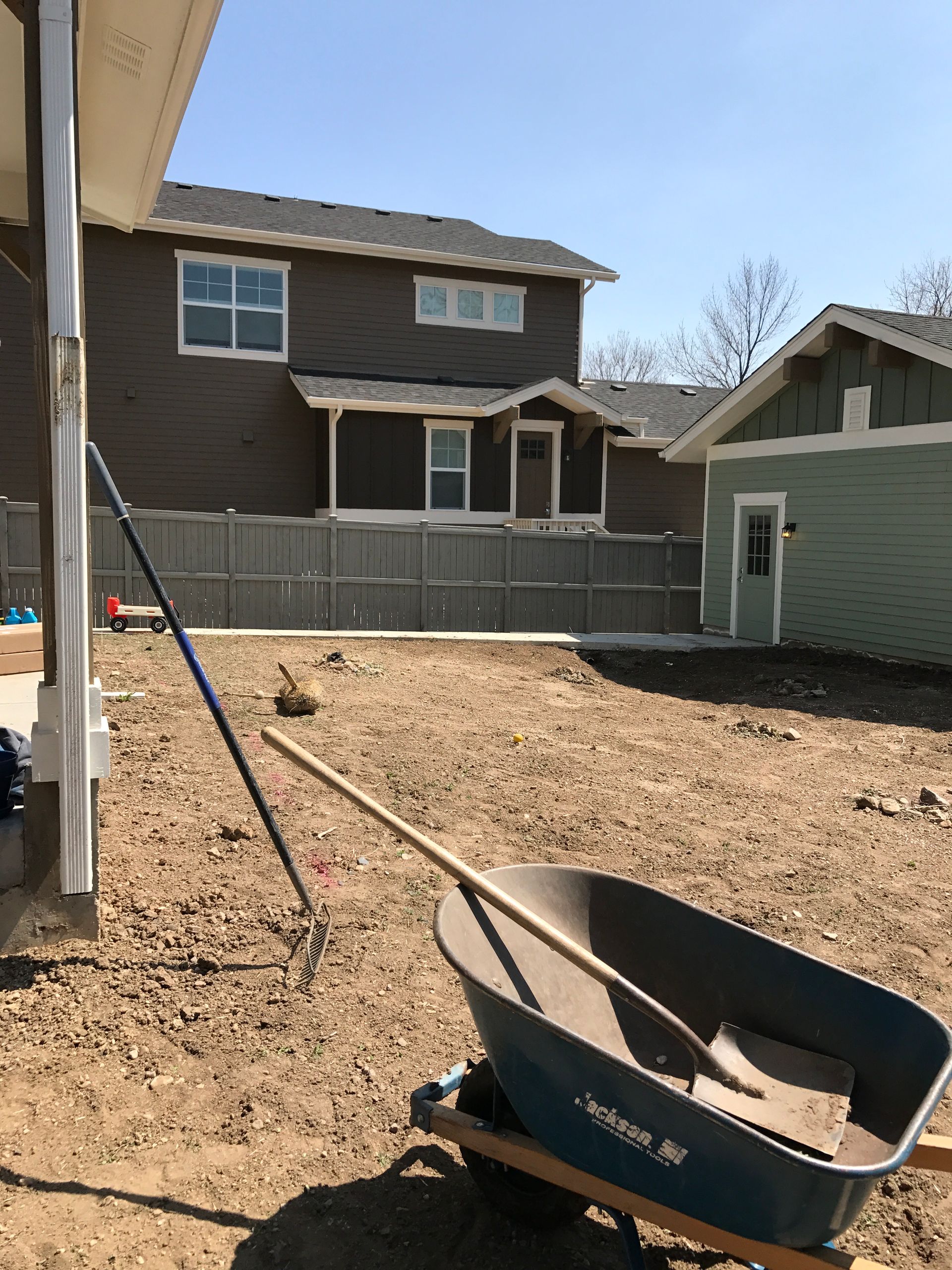 Backyard construction with wheelbarrow, rake, and house in background.