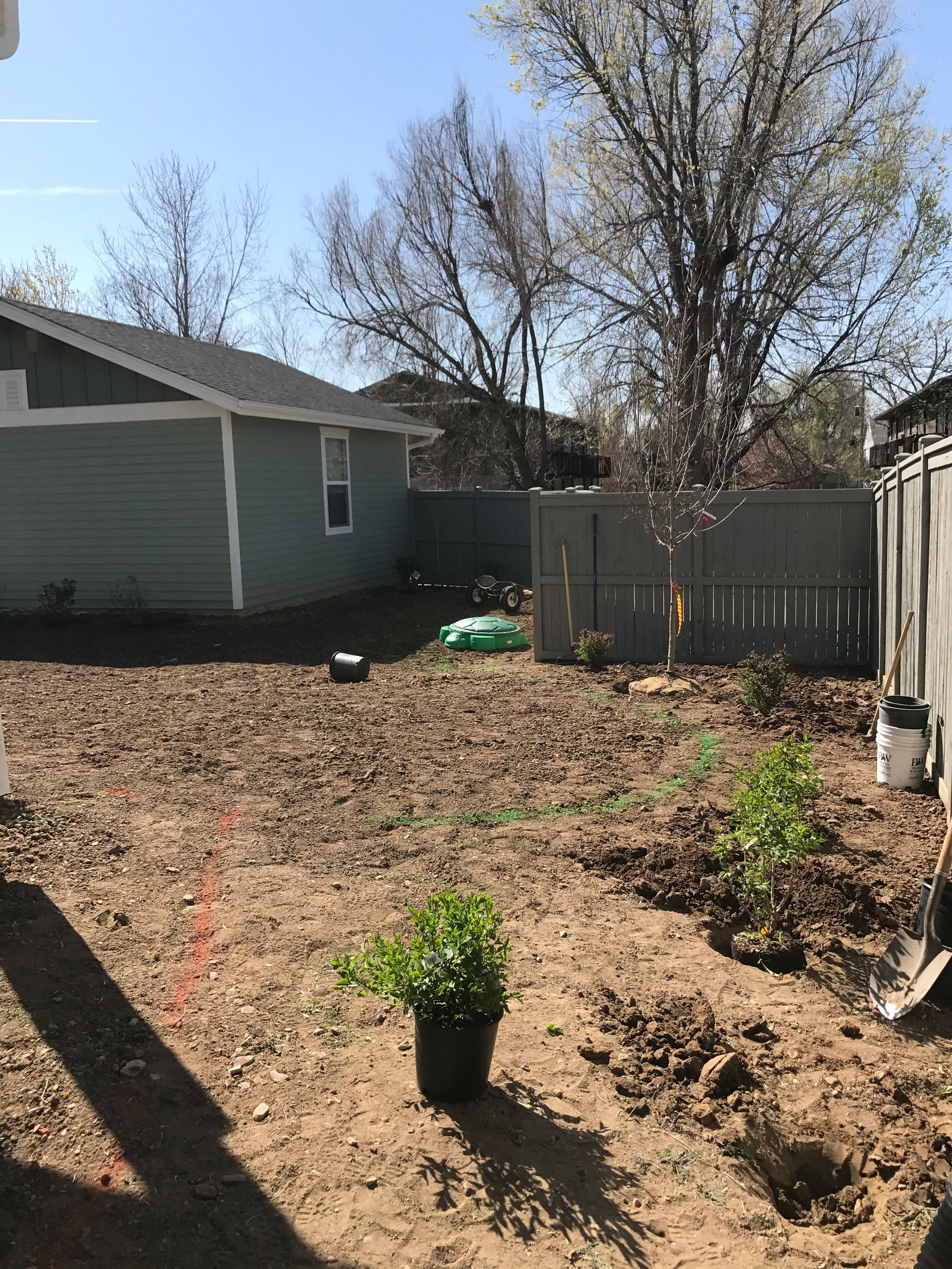A backyard garden being prepared for planting, with a house, fence, and plants in the foreground.