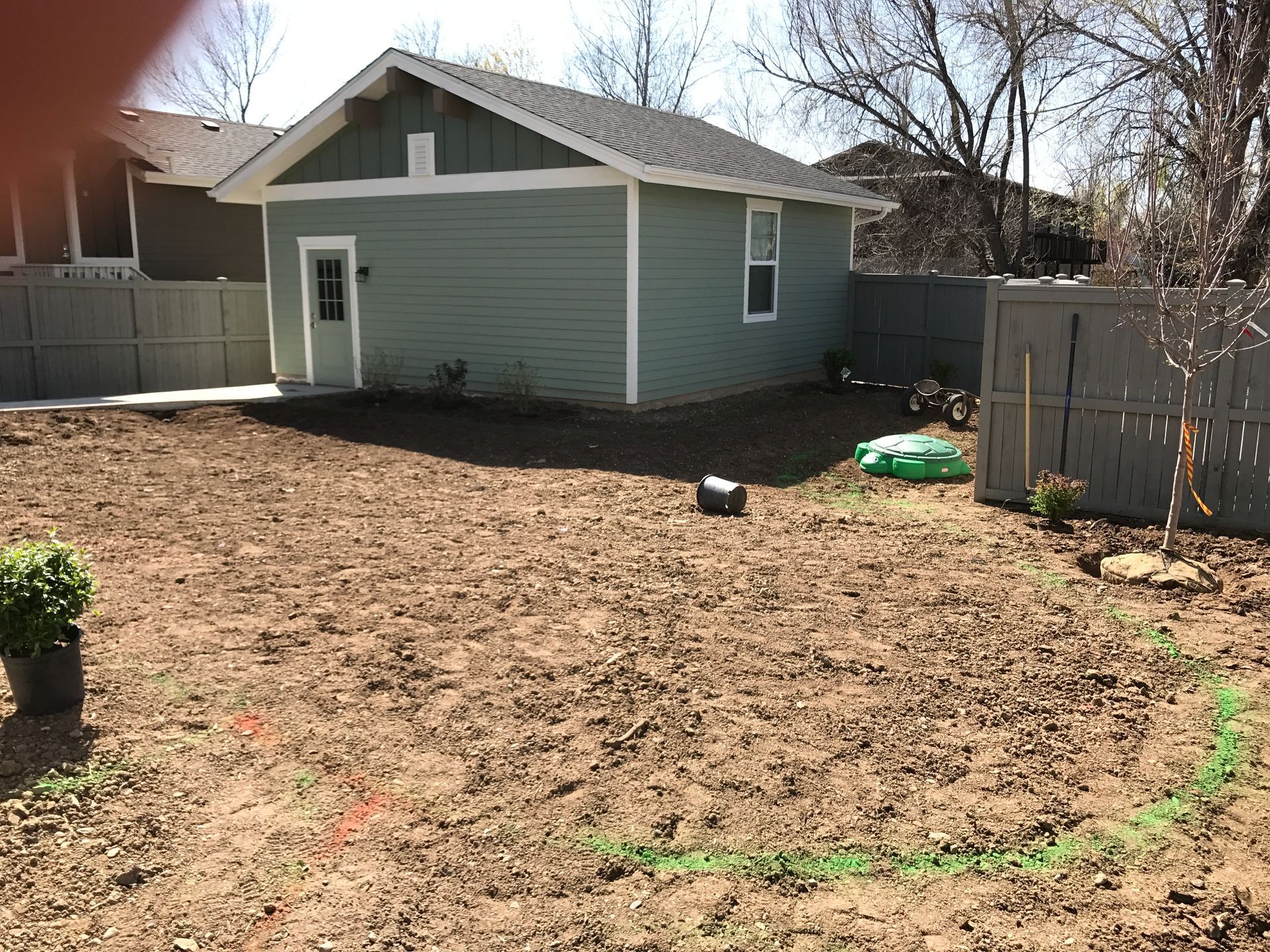 Backyard with a light green outbuilding, brown dirt, and a gray fence.