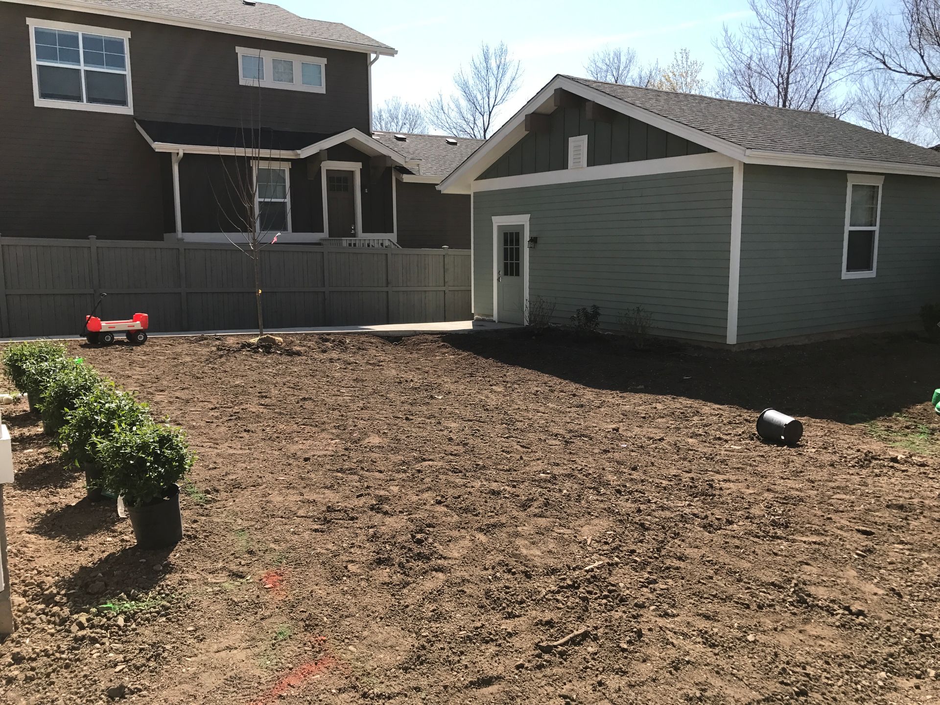 Backyard with a freshly tilled garden bed and green garage. Row of bushes on the left.