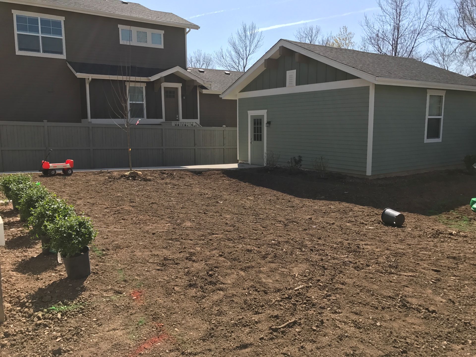 Backyard with freshly tilled soil, a row of green bushes, and a green outbuilding.