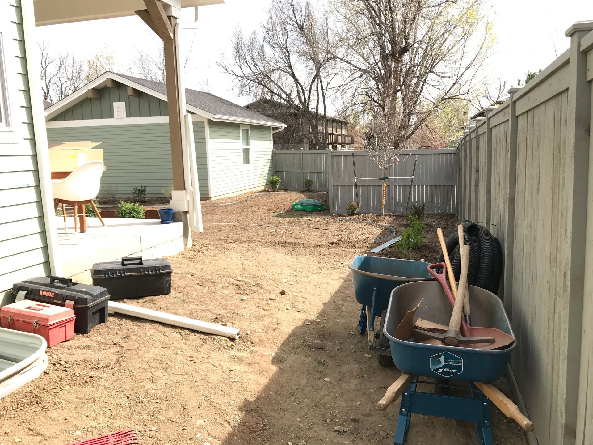 Backyard with dirt, tools, fence, shed, and blue wheelbarrows.