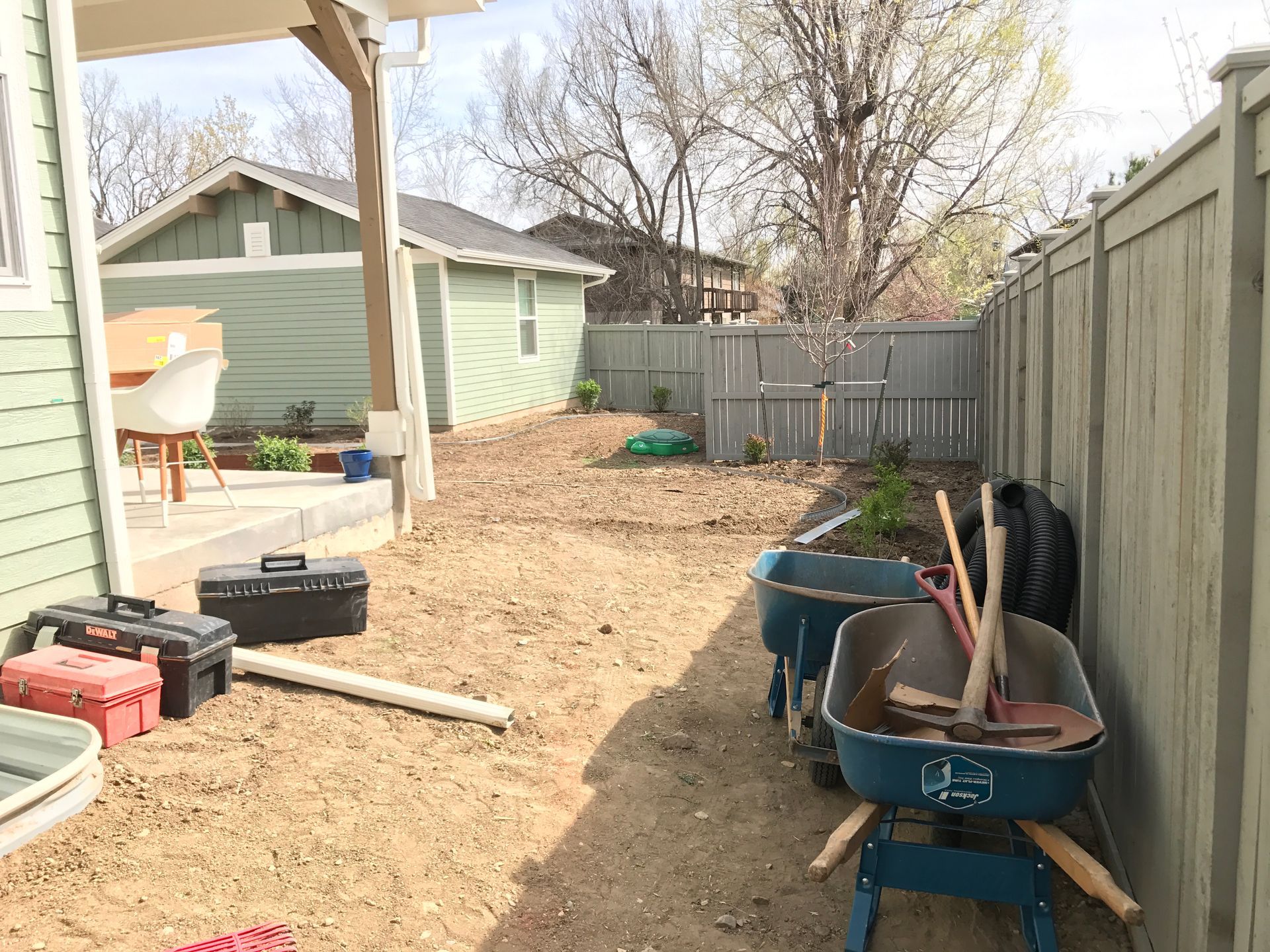 Backyard with tools, wheelbarrows, fence, and a green shed.
