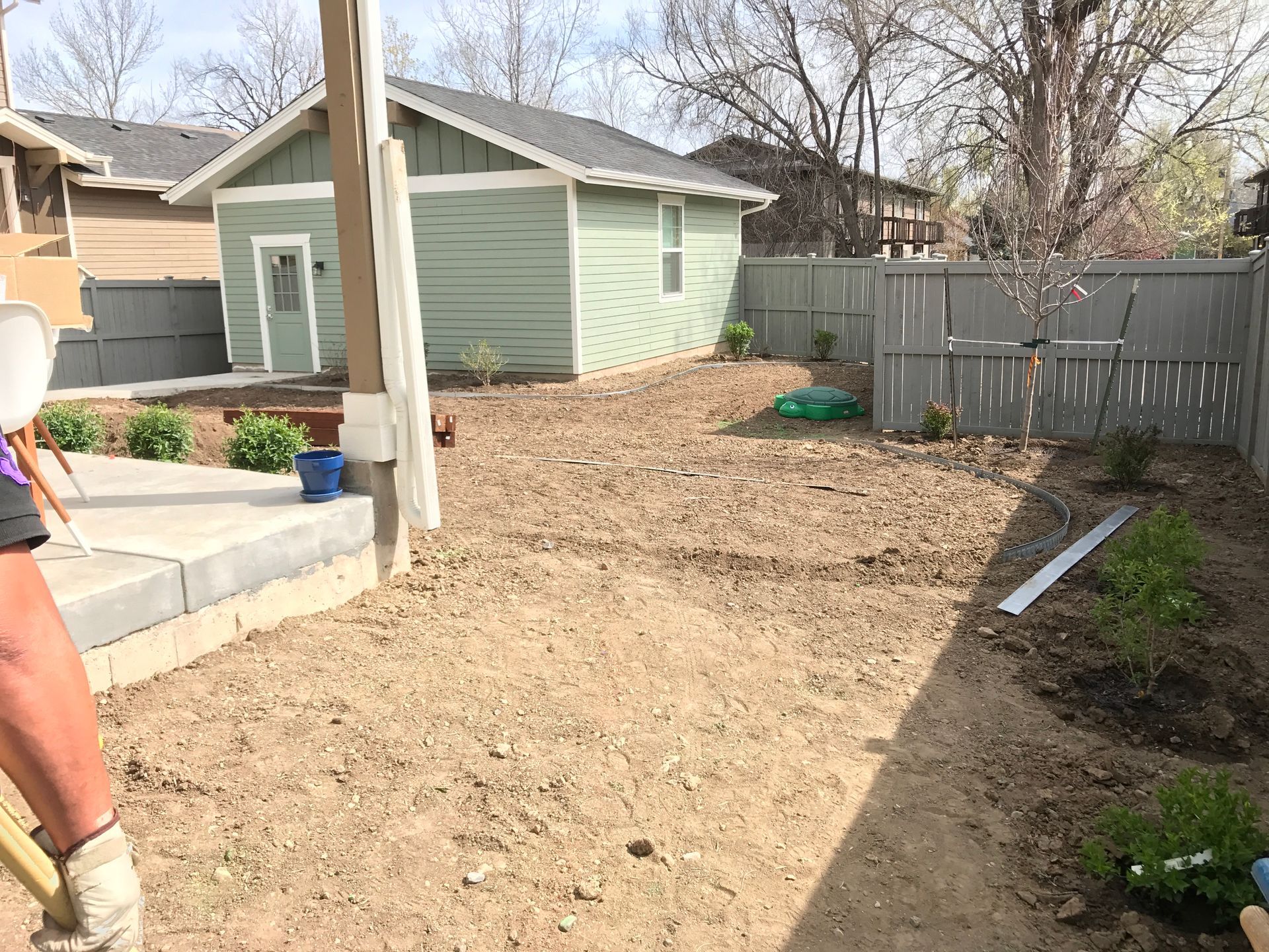 Backyard with dirt, landscaping, shed, fence, and patio. Preparing ground for plants on a sunny day.