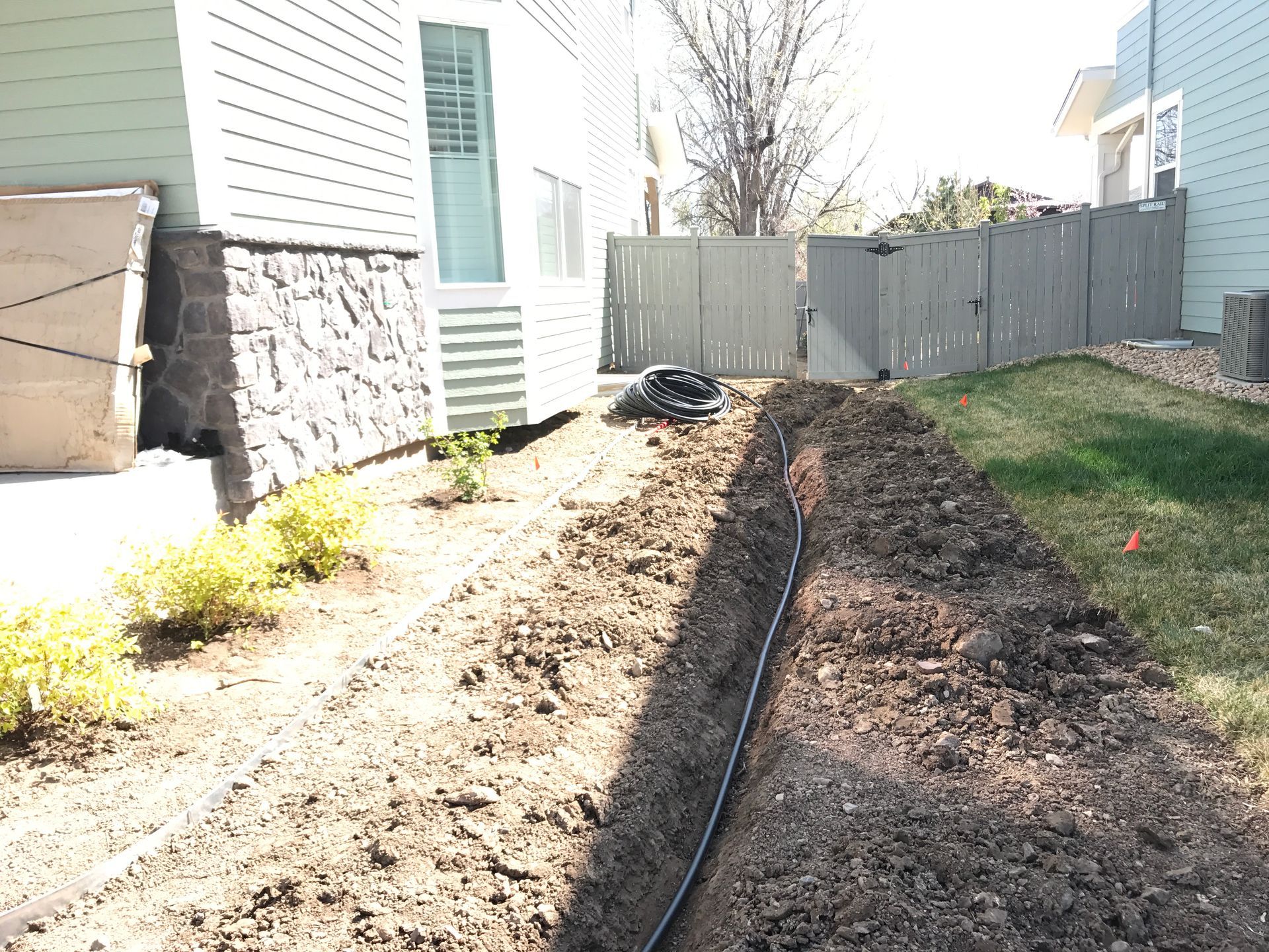 A trench dug in a yard with a black pipe running through it, likely for utilities or irrigation.