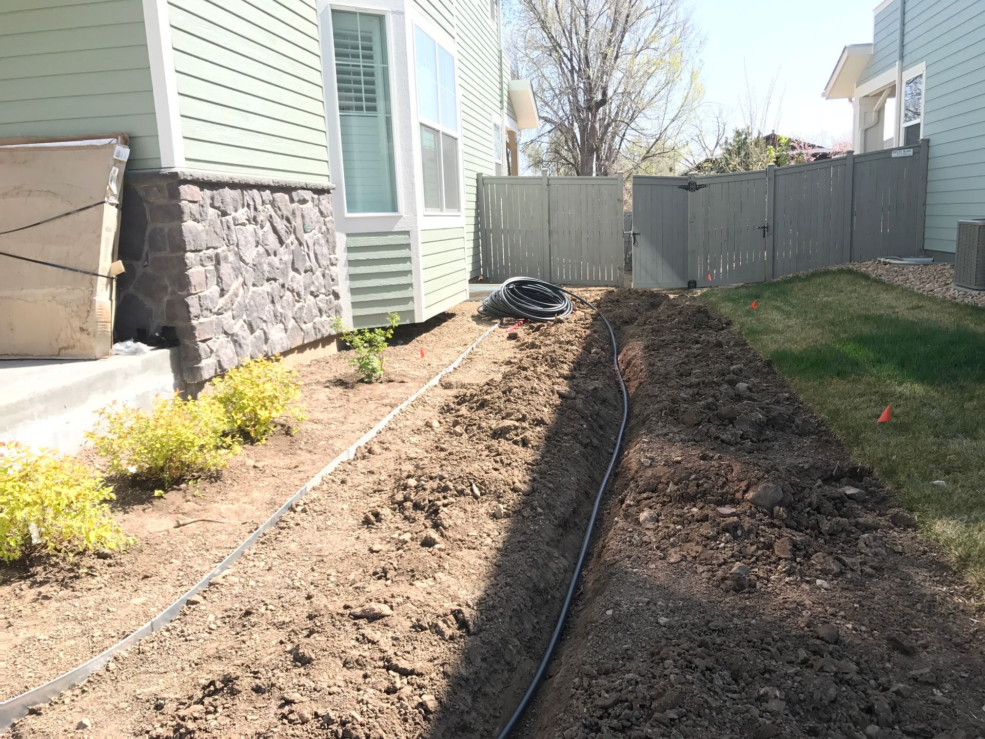 A trench dug alongside a house, with irrigation pipes laid in the soil.