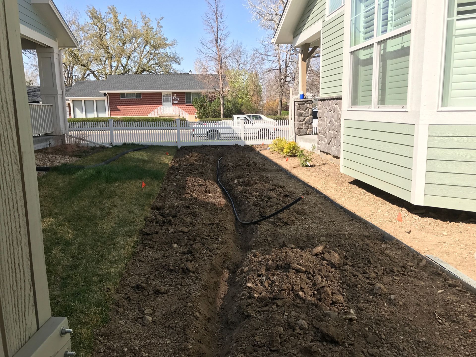 A trench dug in a yard between two buildings, preparing for planting.