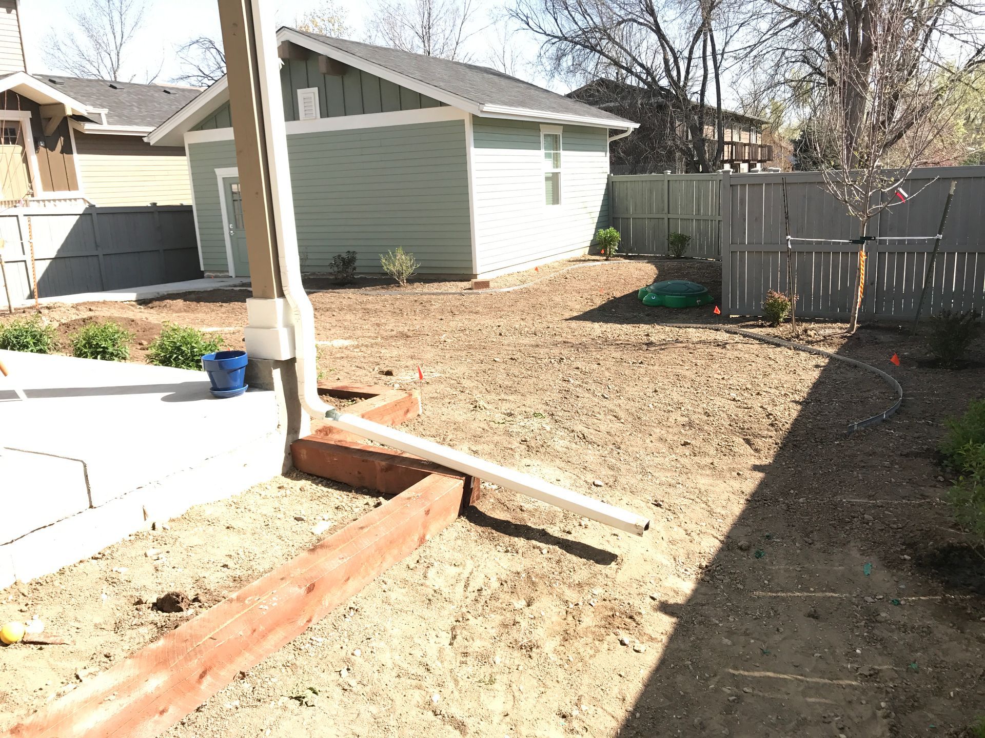 Backyard with dirt, shed, fence, concrete patio, wooden border, and blue bucket.