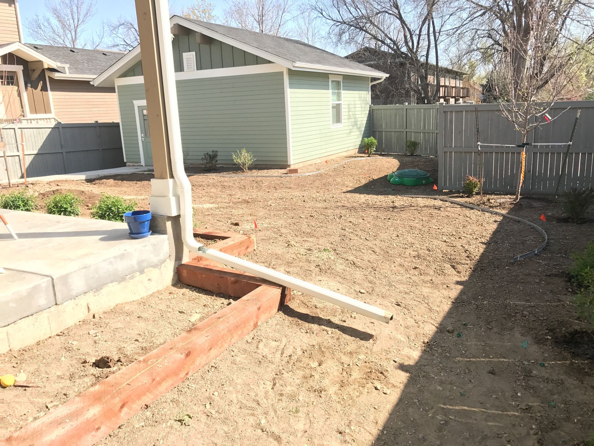 Backyard with dirt, green shed, wooden fence, red planter, and blue bucket.