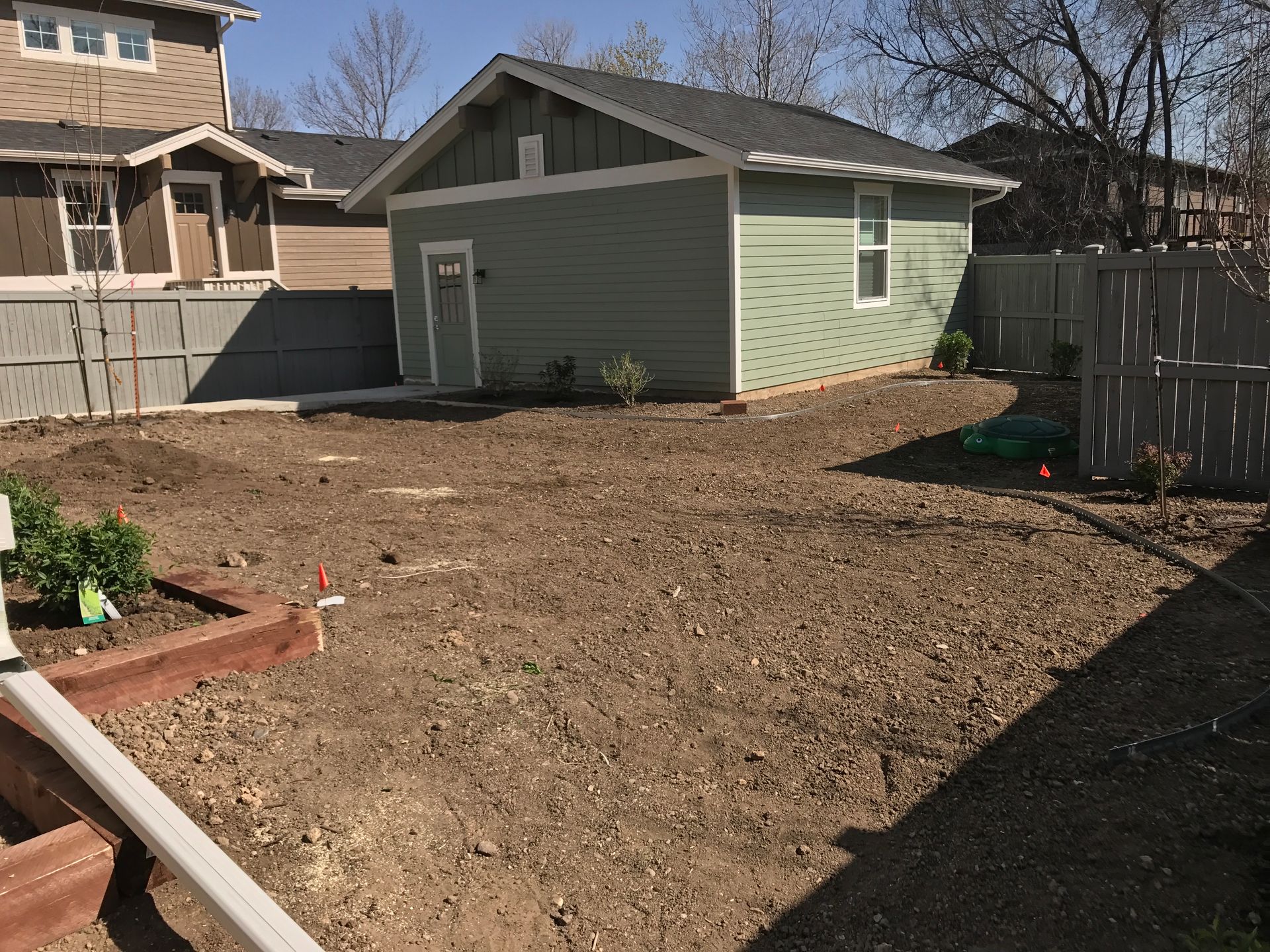 Backyard with a small green building, dirt ground, and a wooden fence.