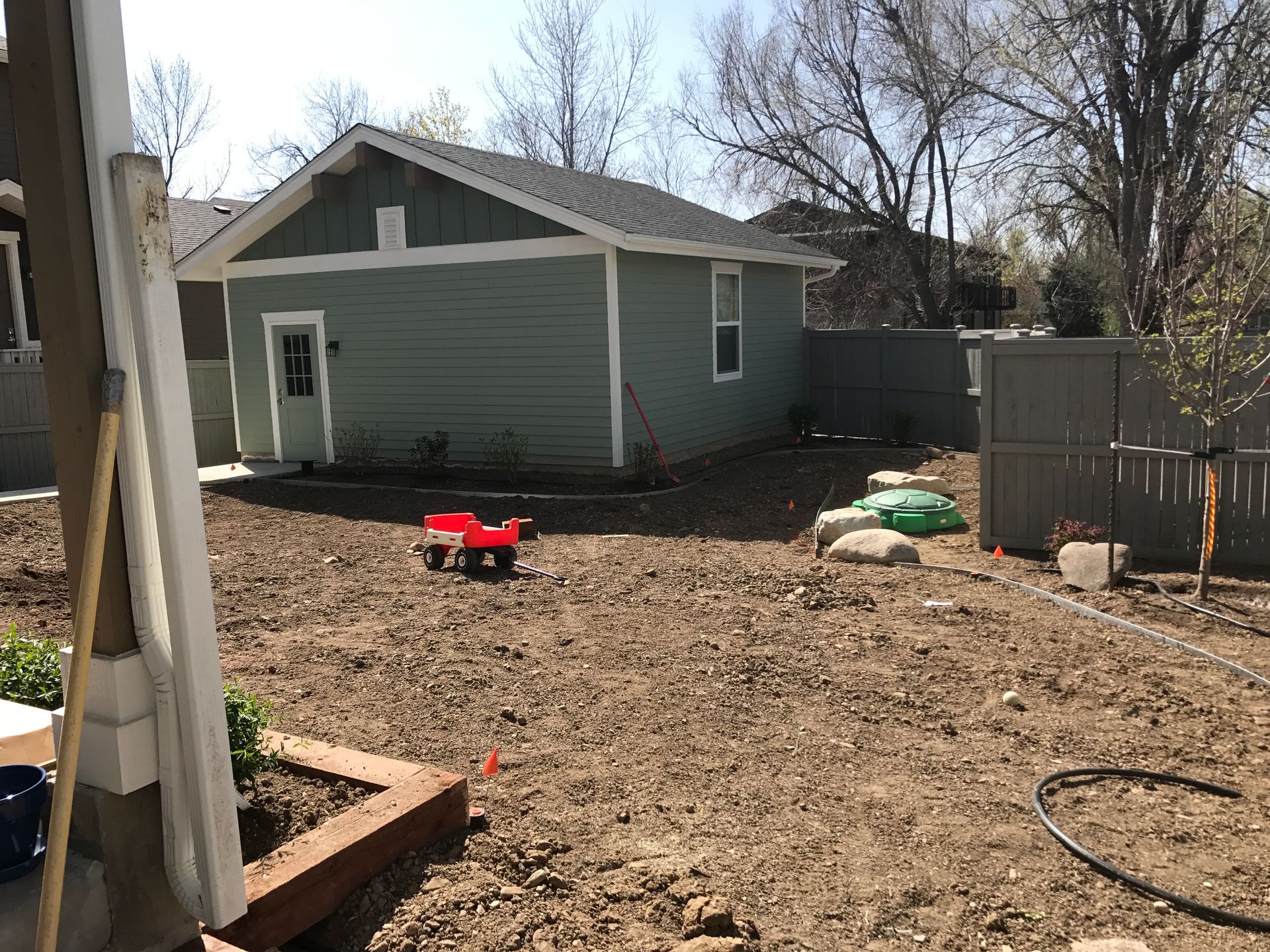 A backyard with bare earth, a green shed, a red wagon, and a gray fence.