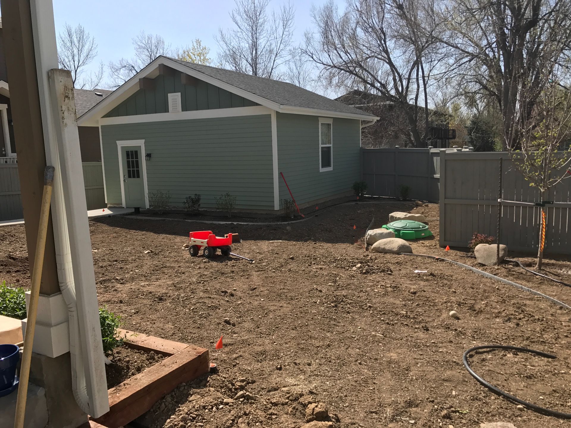 Backyard with a green building, red toy wagon, and brown soil.