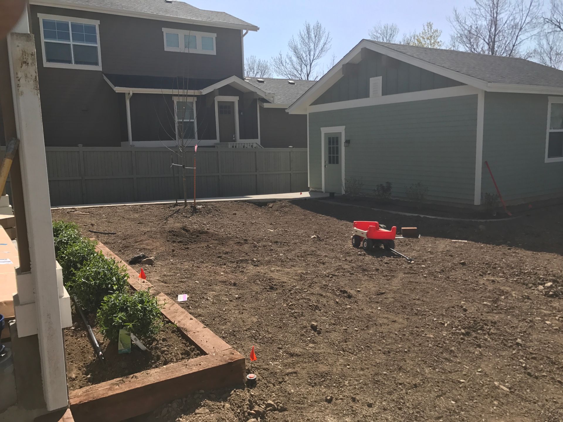 Backyard with dirt ground, a small wagon, and green shed next to a two-story house.