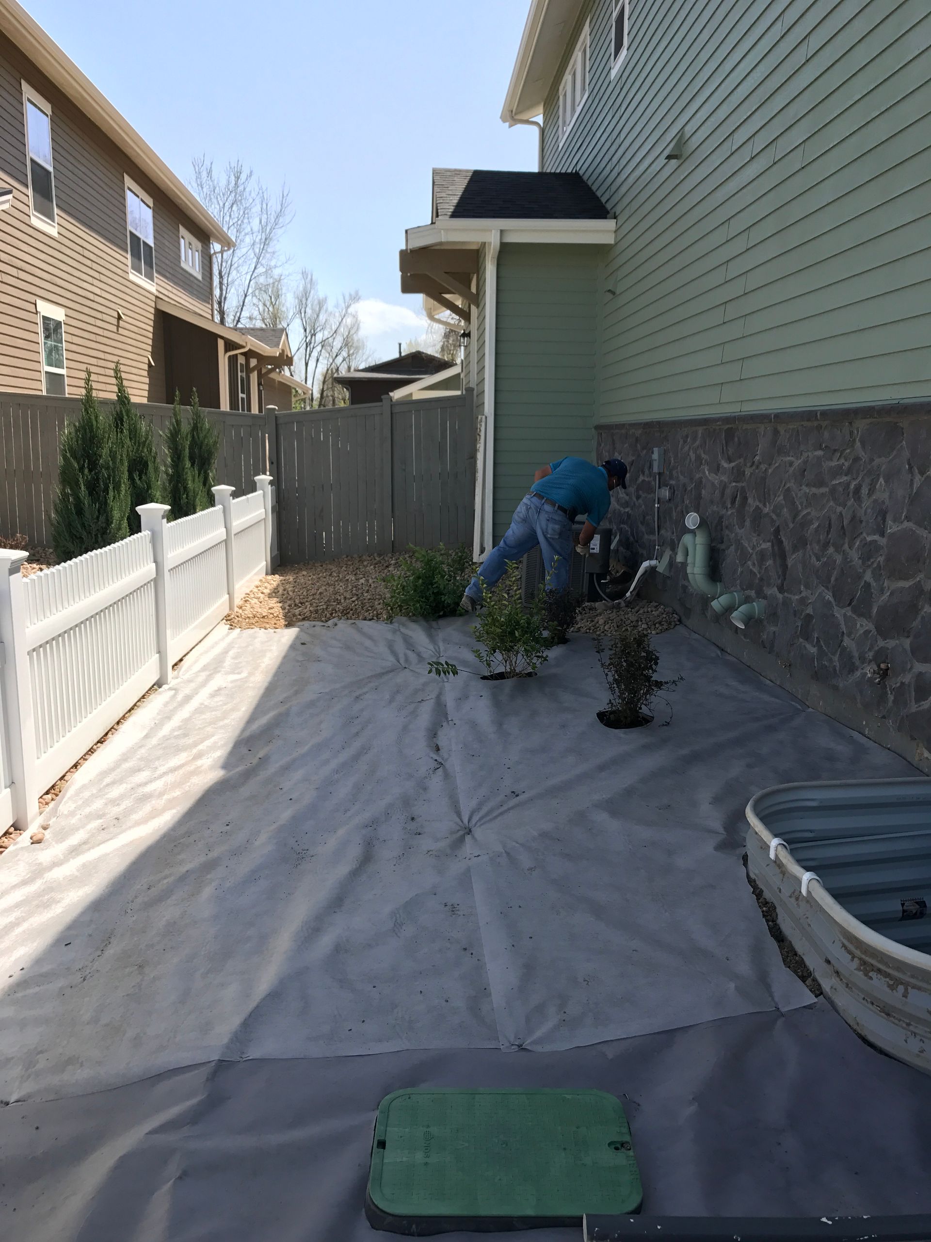 Person planting flowers in a backyard garden, next to a house with a gray fence and a boat.