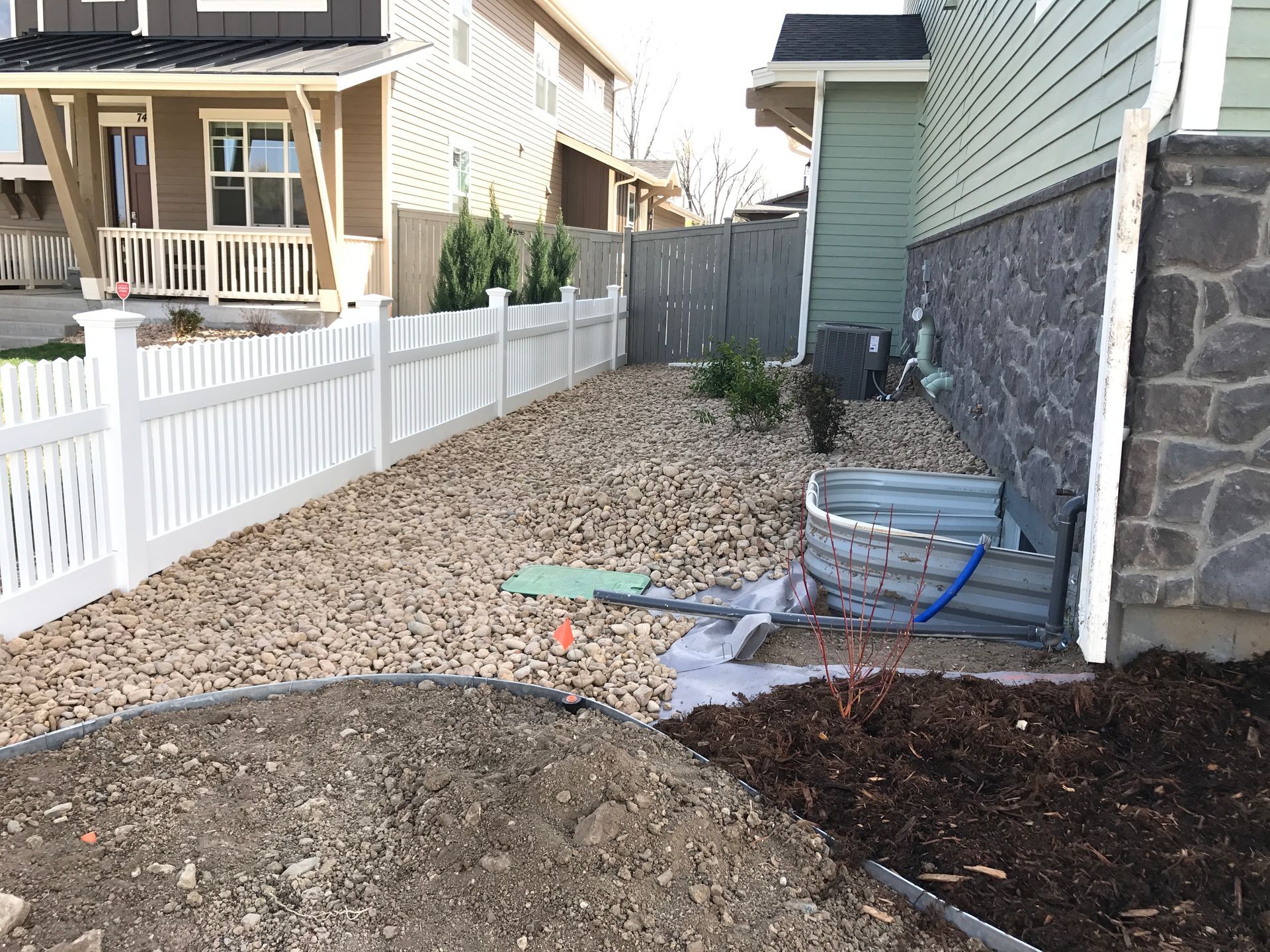 Side yard with white fence, rocks, and foundation with window well.