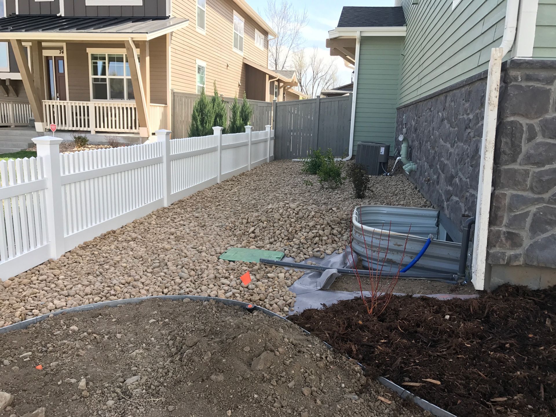 Side yard with white fence, rocks, and house foundation with stone facade.