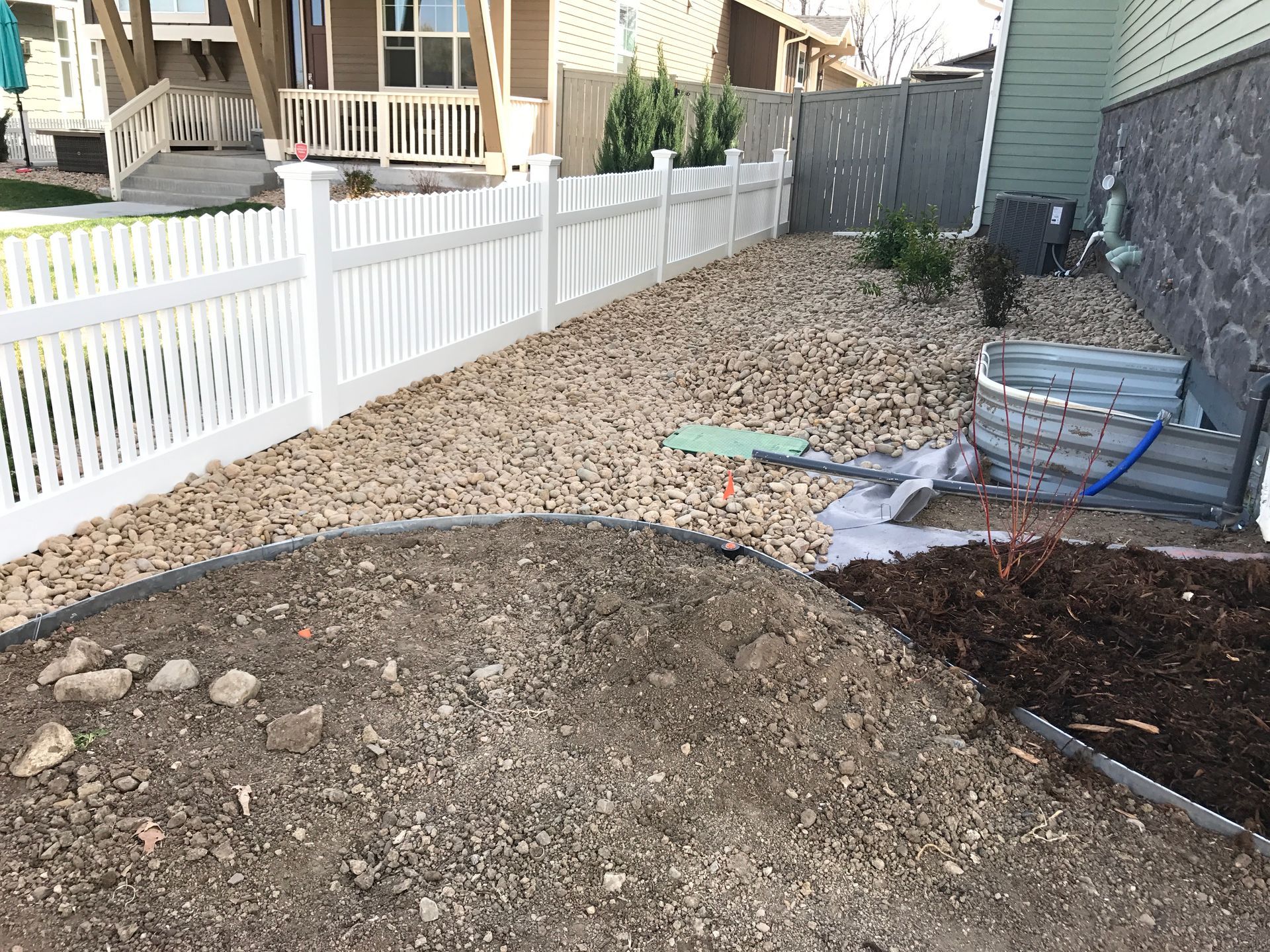A yard with white fence and rock ground cover. A dirt pile in the foreground.