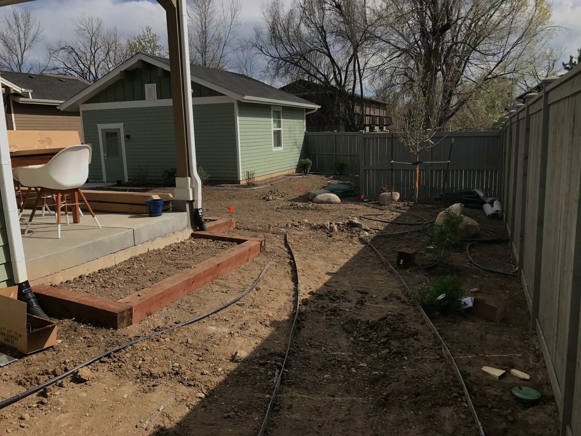 Backyard with dirt and dry grass. Wood fence, shed, and deck with chairs are visible.